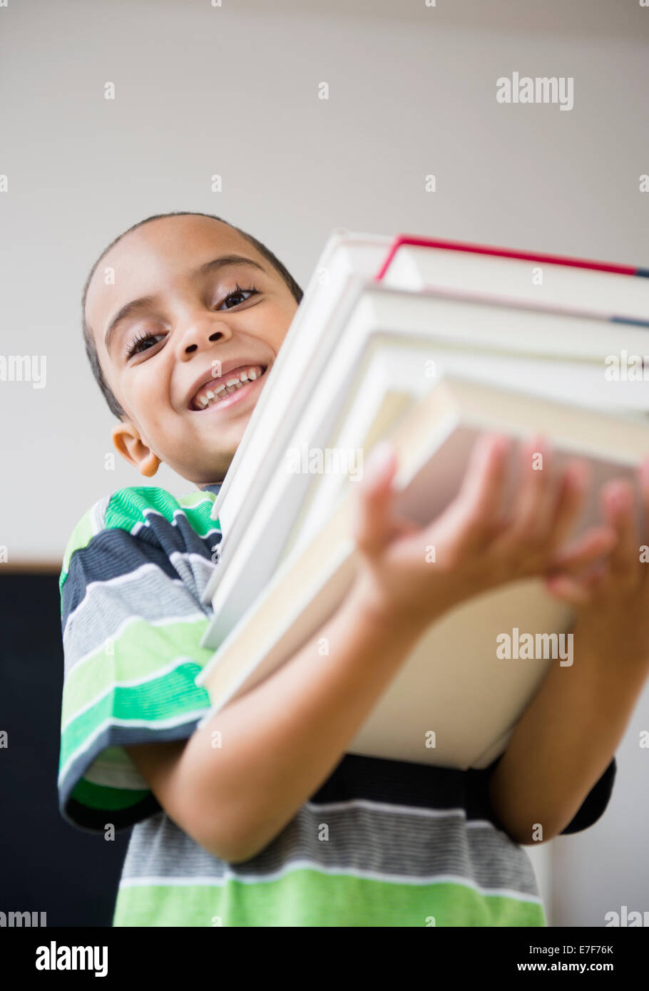 Mixed race boy carrying stack of books in class Stock Photo