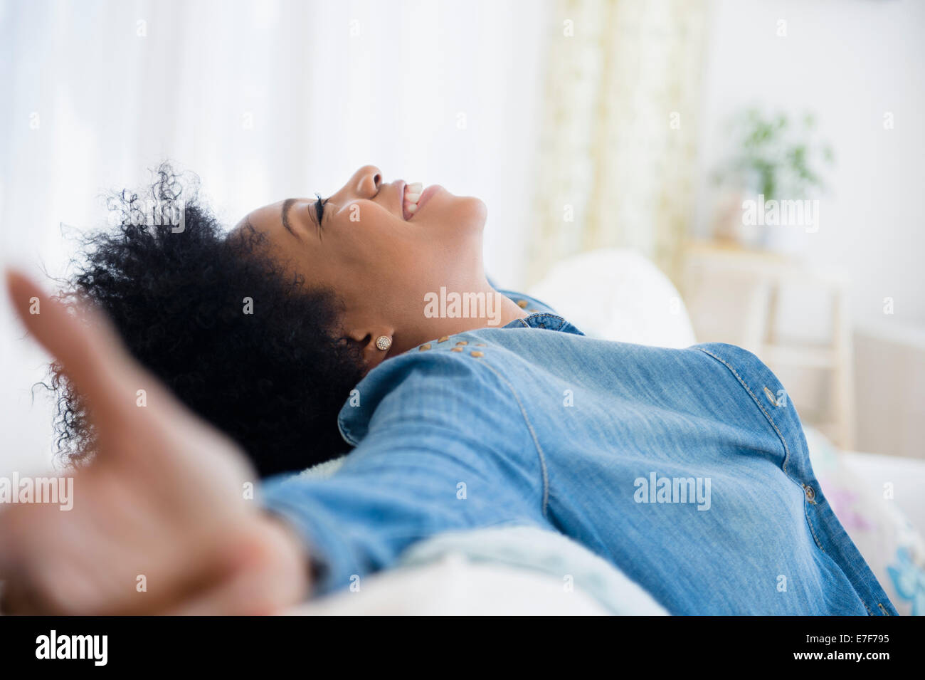 African American woman with arms outstretched on sofa Stock Photo