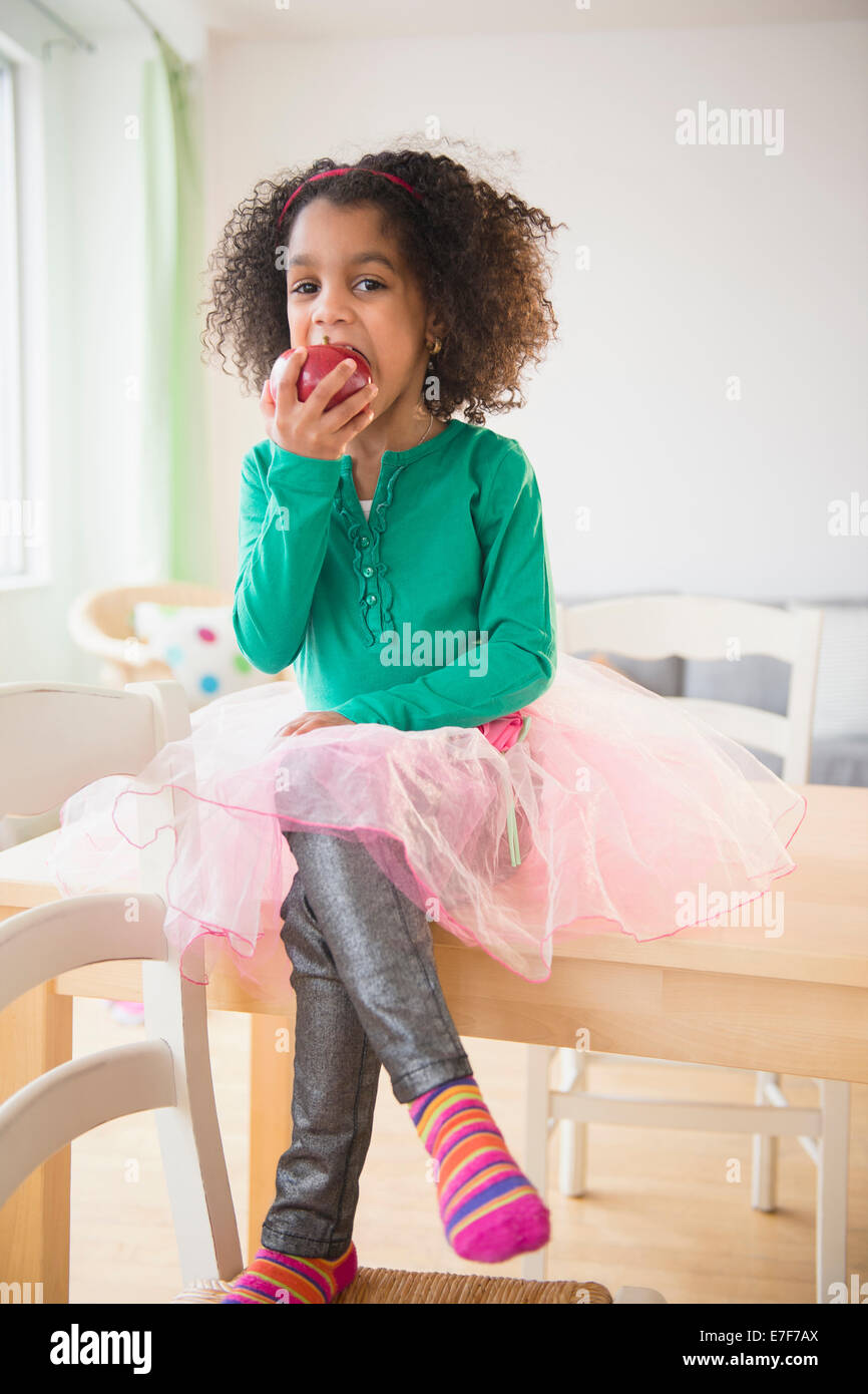African American girl eating apple at kitchen table Stock Photo