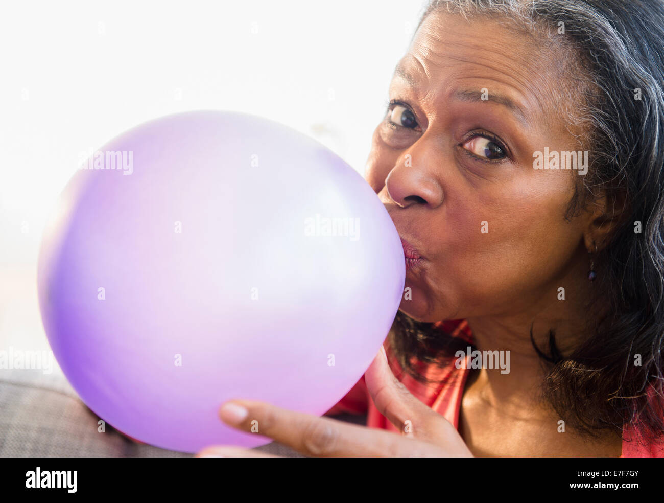 Mixed race woman blowing balloon on sofa Stock Photo