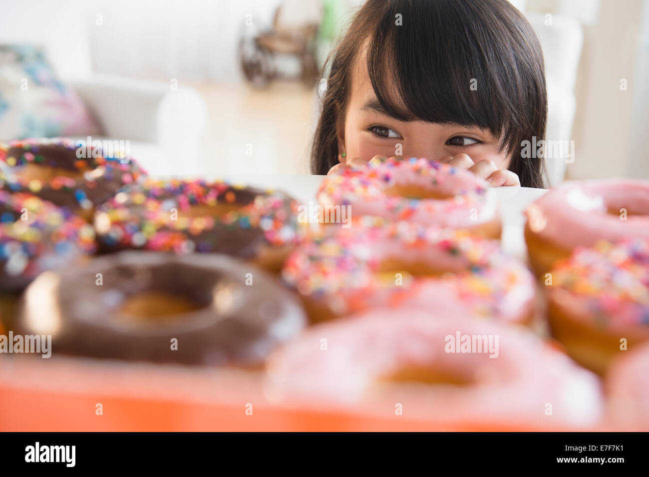 Filipino girl peering at donuts on table Stock Photo