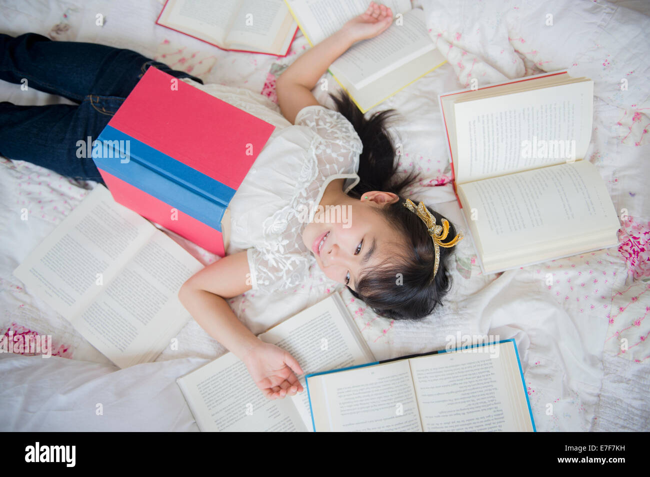 Filipino girl laying in bed with books Stock Photo