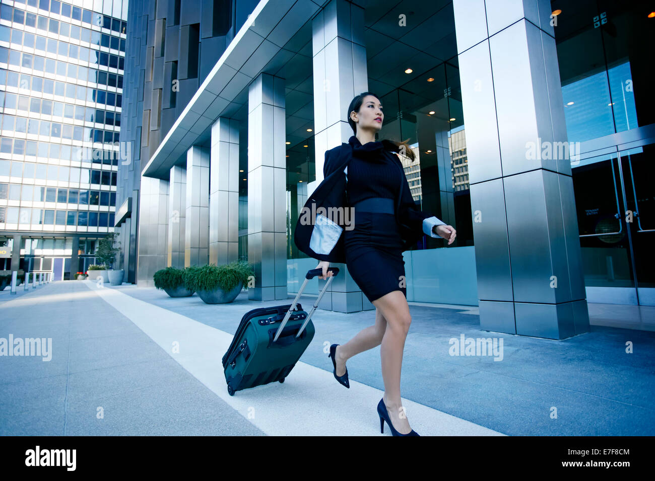 Mixed race businesswoman rolling baggage in city Stock Photo