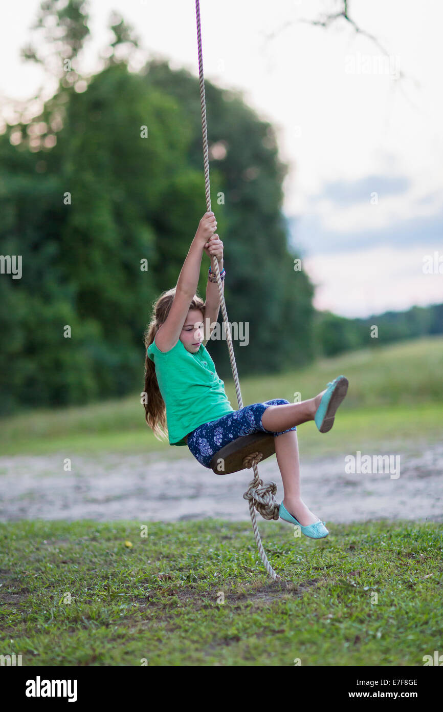 Caucasian girl playing on rope swing Stock Photo
