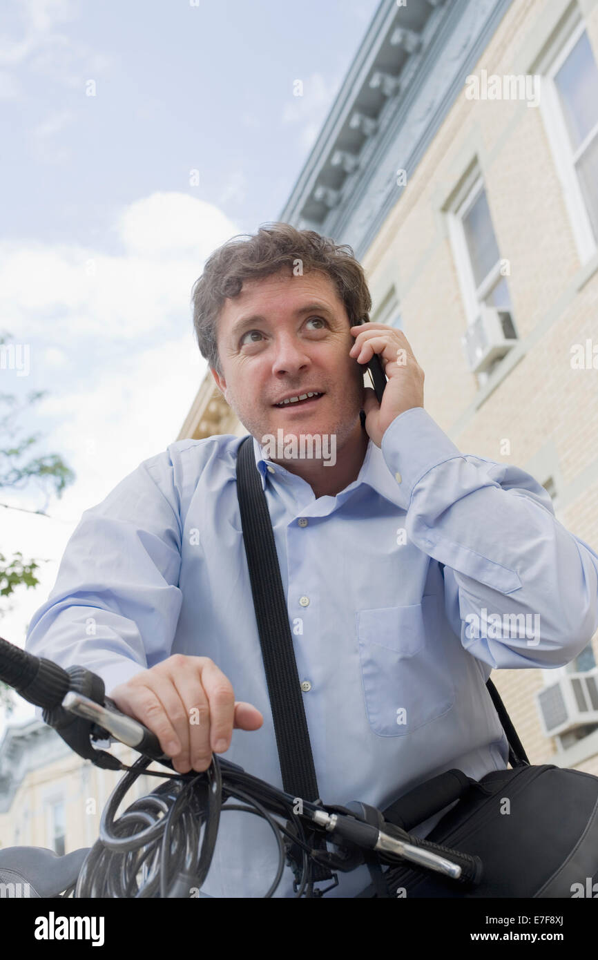 Hispanic businessman talking on cell phone on bicycle on city street Stock Photo
