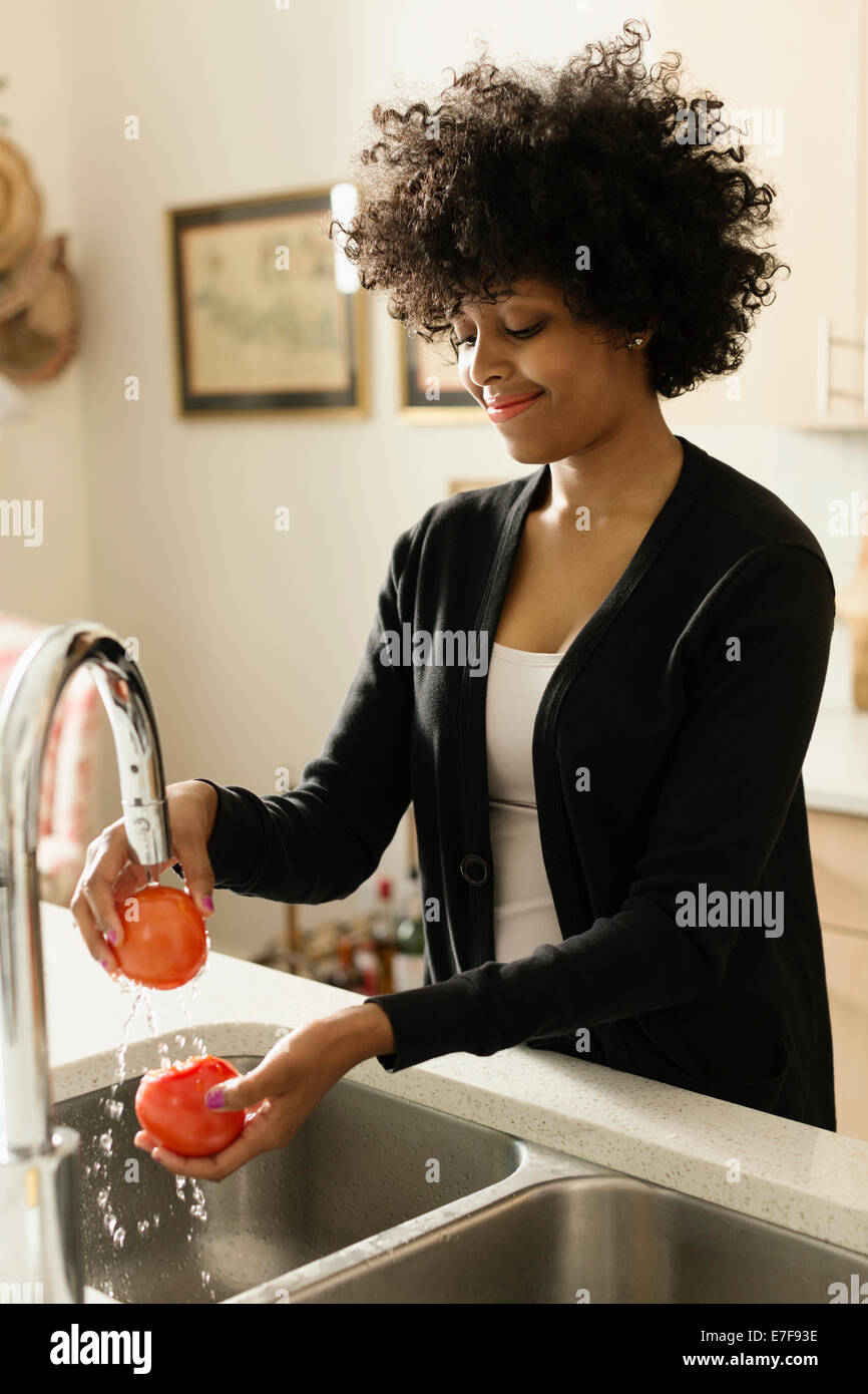 Mixed race woman washing tomatoes in kitchen Stock Photo