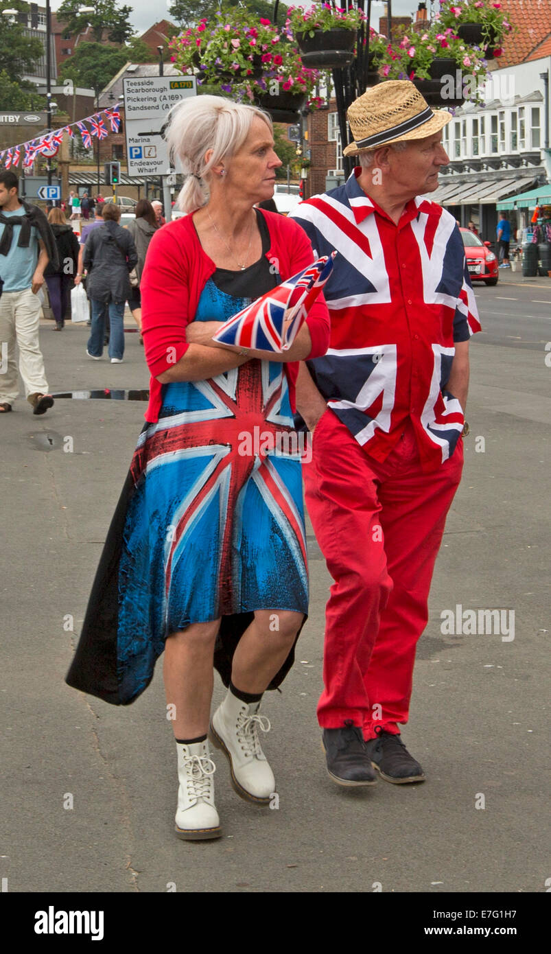 Elderly couple dressed in bright and unusual clothes made from Union Jack British flag and carrying flag at Whitby England Stock Photo