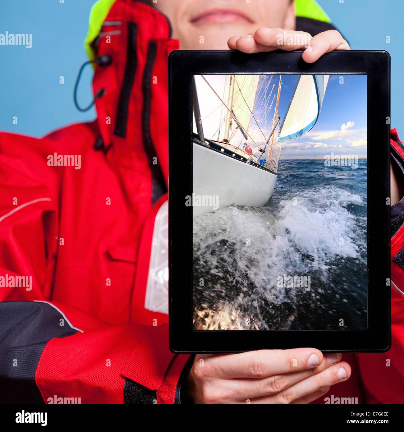 Man in wind jacket holding ipad with photo of yacht sailboat. Sailor showing screen tablet touchpad dreaming about yachting sail Stock Photo