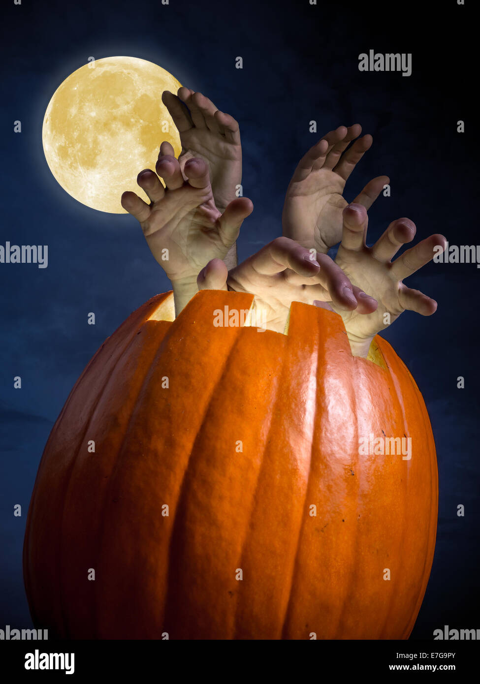 Giant hollow pumpkin with protruding zombi hands shot against full moon night sky Stock Photo