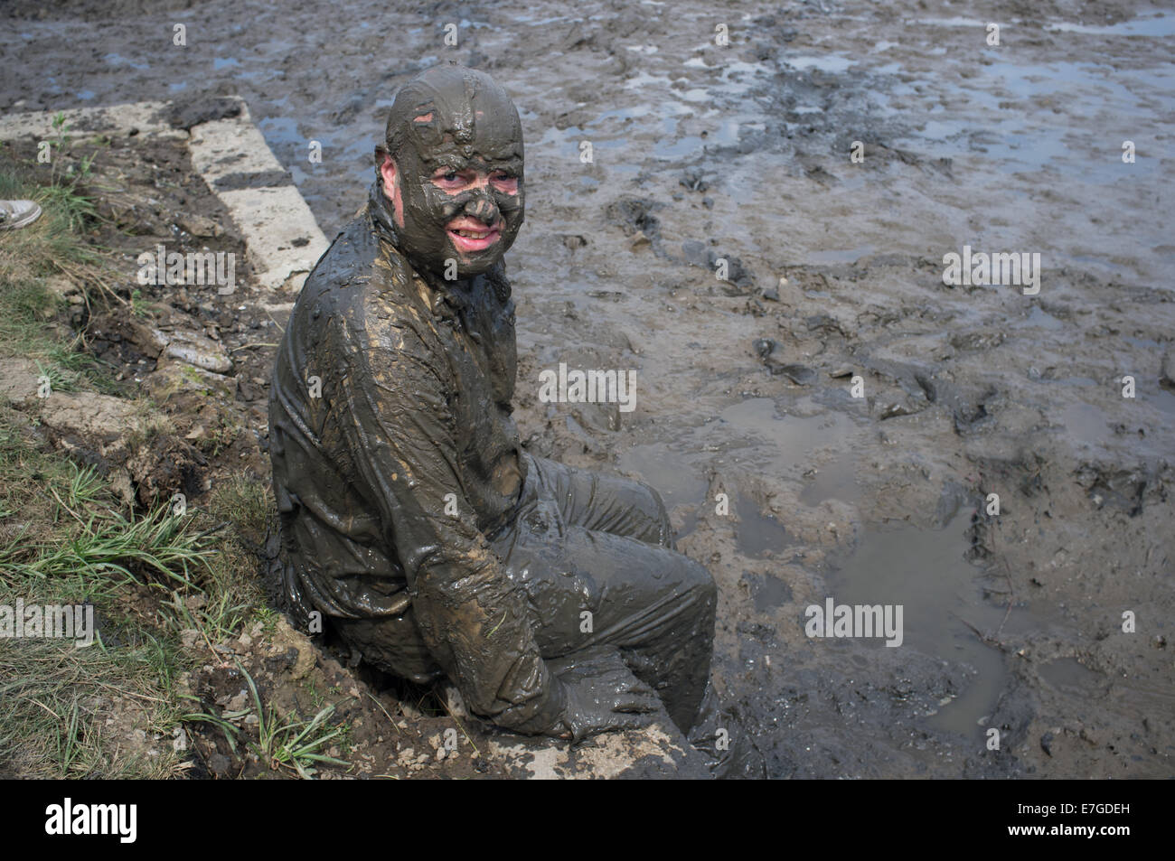 A clothed man sitting in a muddy estuary at the Port Eliot festival. Stock Photo