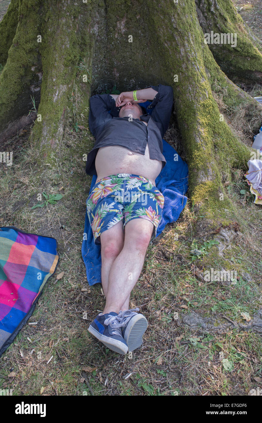 An overweight man asleep under a tree Stock Photo