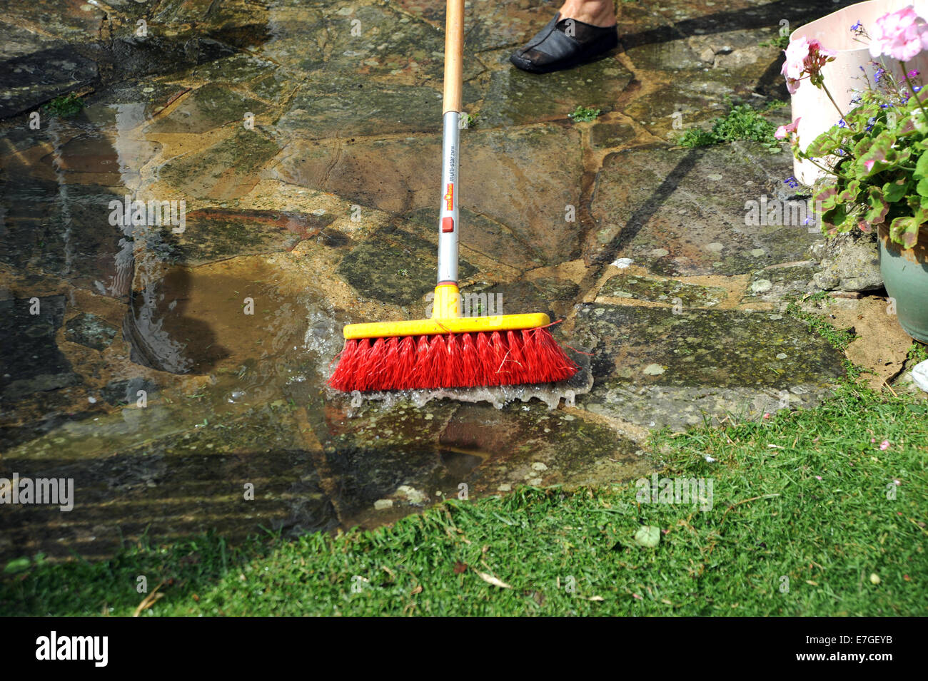 Scrubbing clean a garden patio with orange bristled broom brush and water Stock Photo