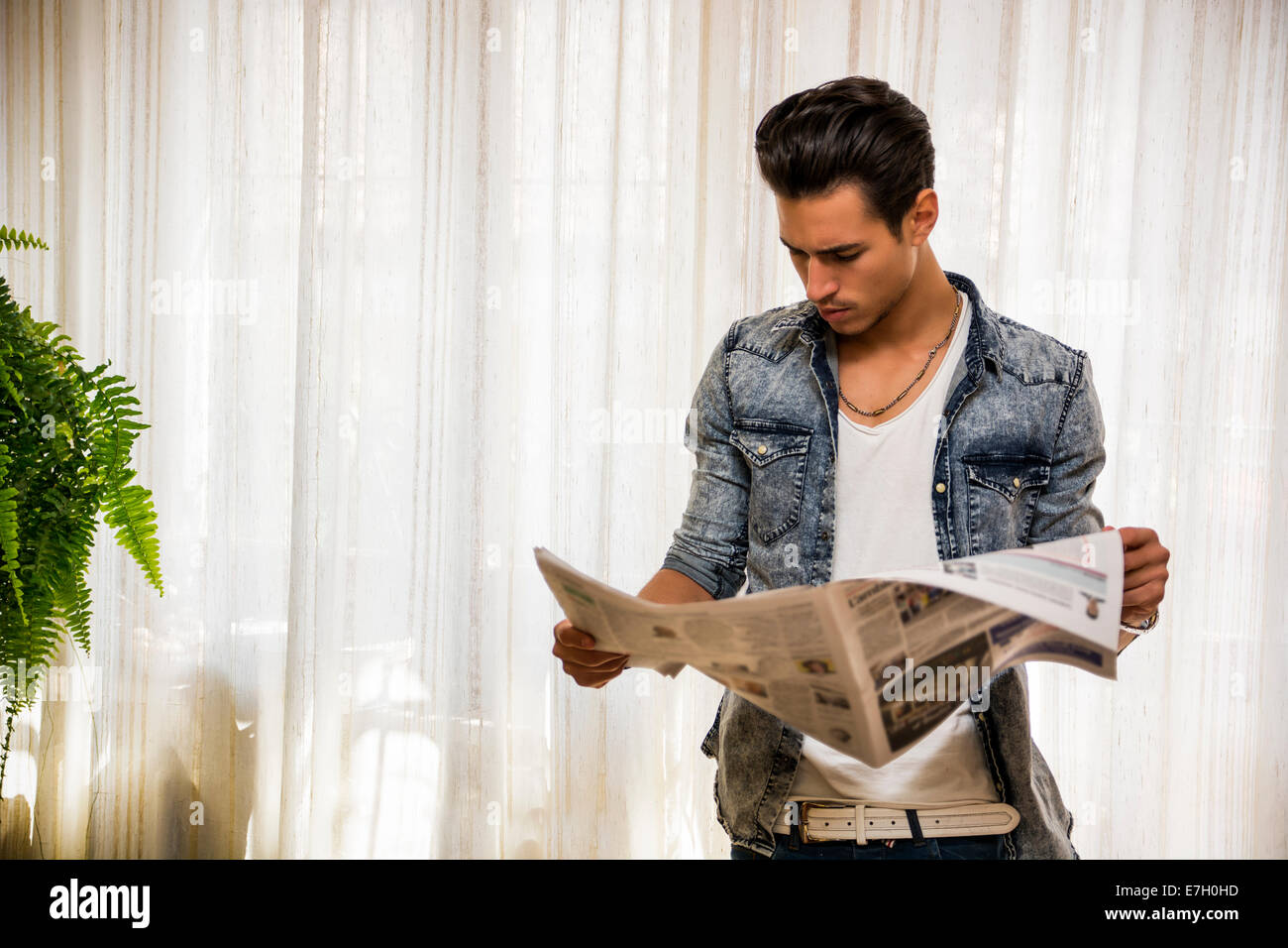 Handsome young man at home reading newspaper, standing Stock Photo - Alamy