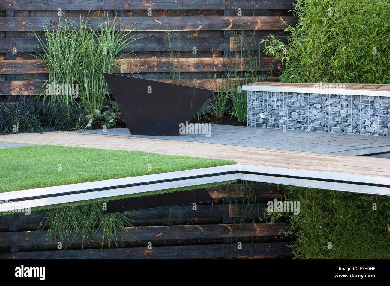 Garden - Elemental - reflective dark pool pond with charred burned redwood board wall basalt cobbles in cage Stock Photo