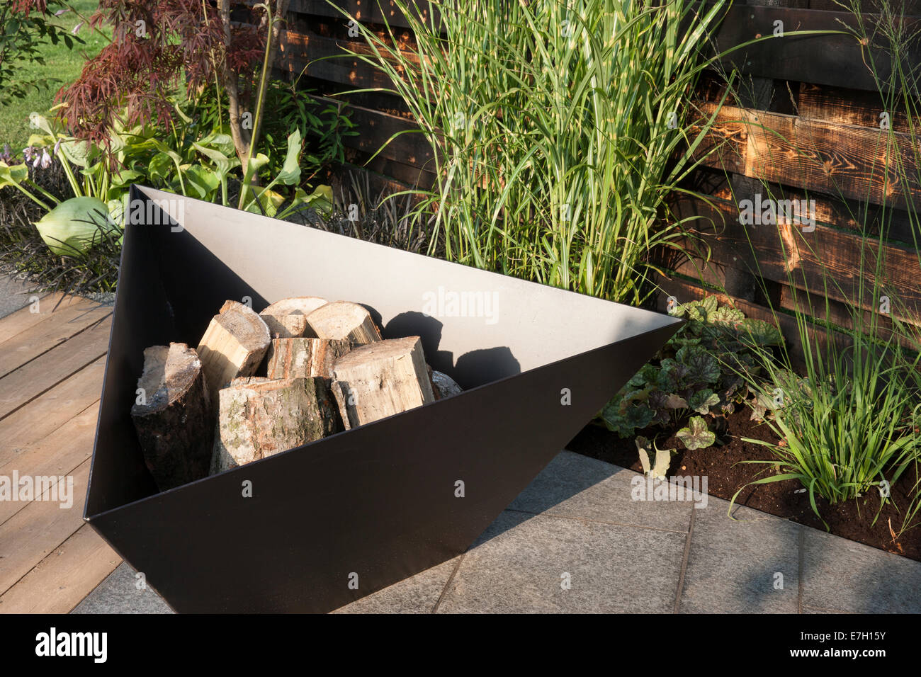 Garden - Elemental - garden fire pit firepit and charred burned redwood timber board wall - basalt patio stone and planting of zebra grass Stock Photo