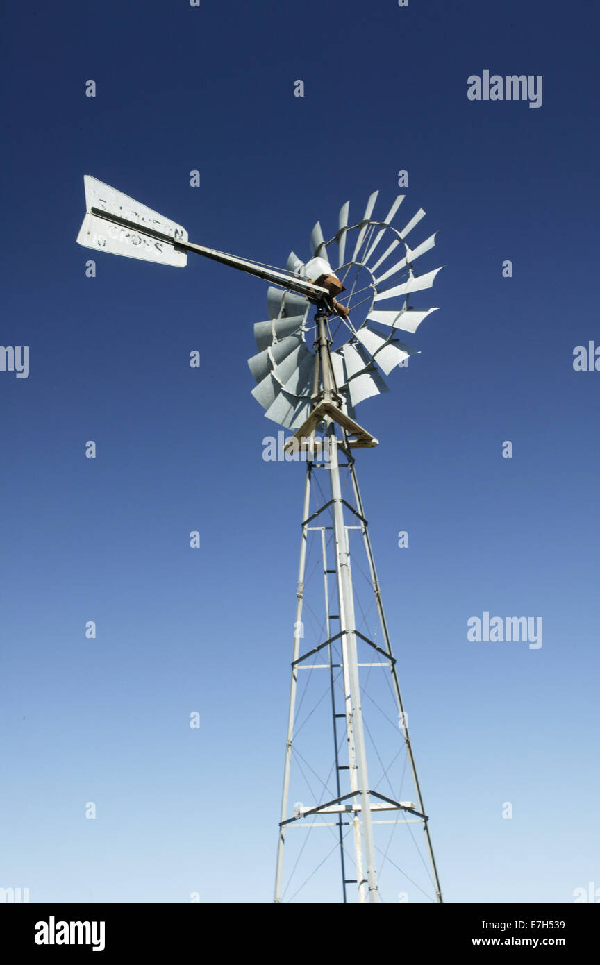 A tall metal windmill against a blue sky on a farm property. Stock Photo