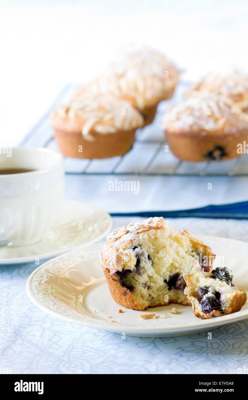 A half-eaten muffin in front of other muffins and a cup of coffee. Stock Photo