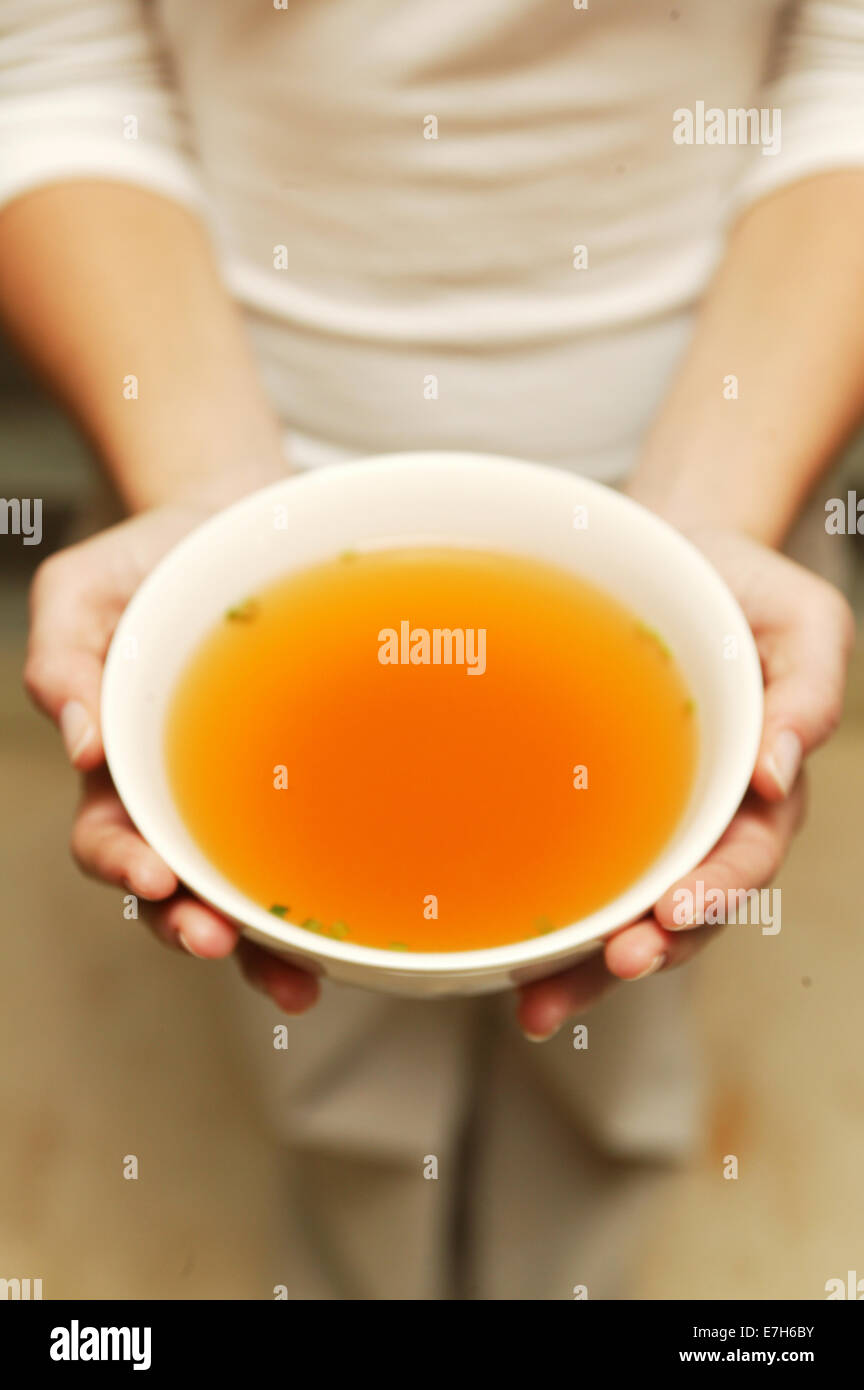 A woman holding a bowl of chicken broth with both hands. Stock Photo