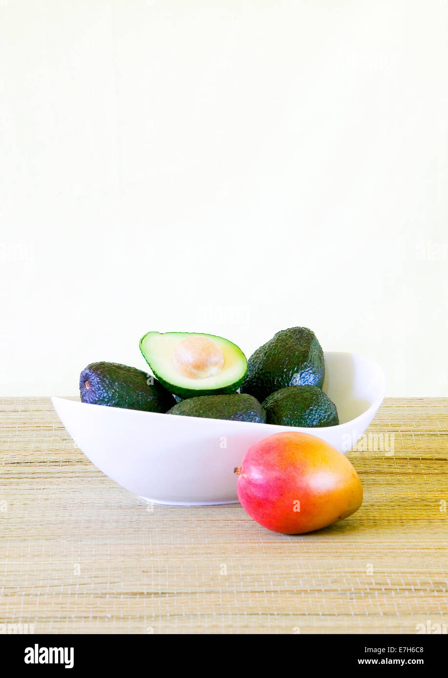 Avocados in a white bowl next to a mango. Stock Photo