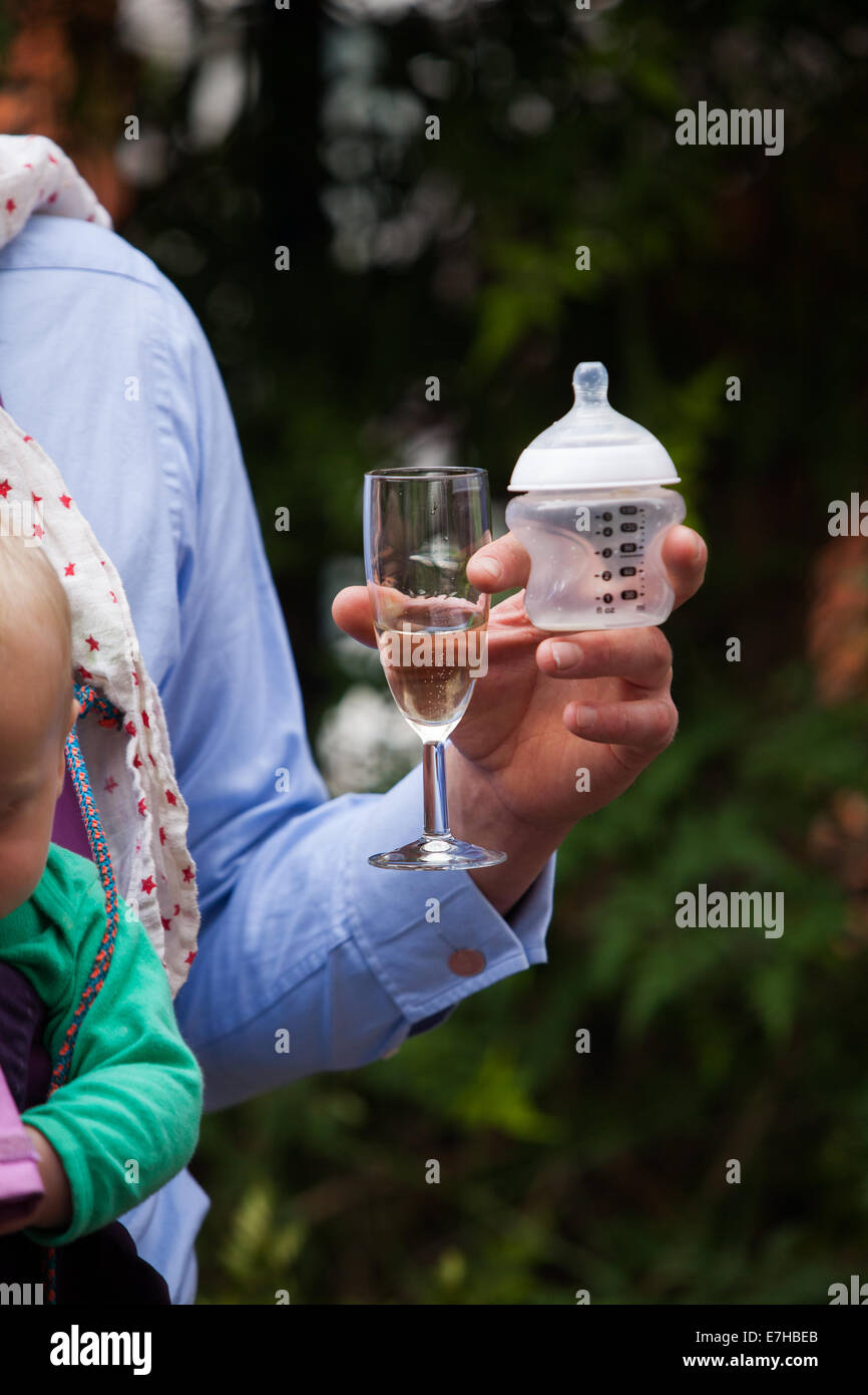 Father's hand holding baby bottle and glass of champagne Stock Photo