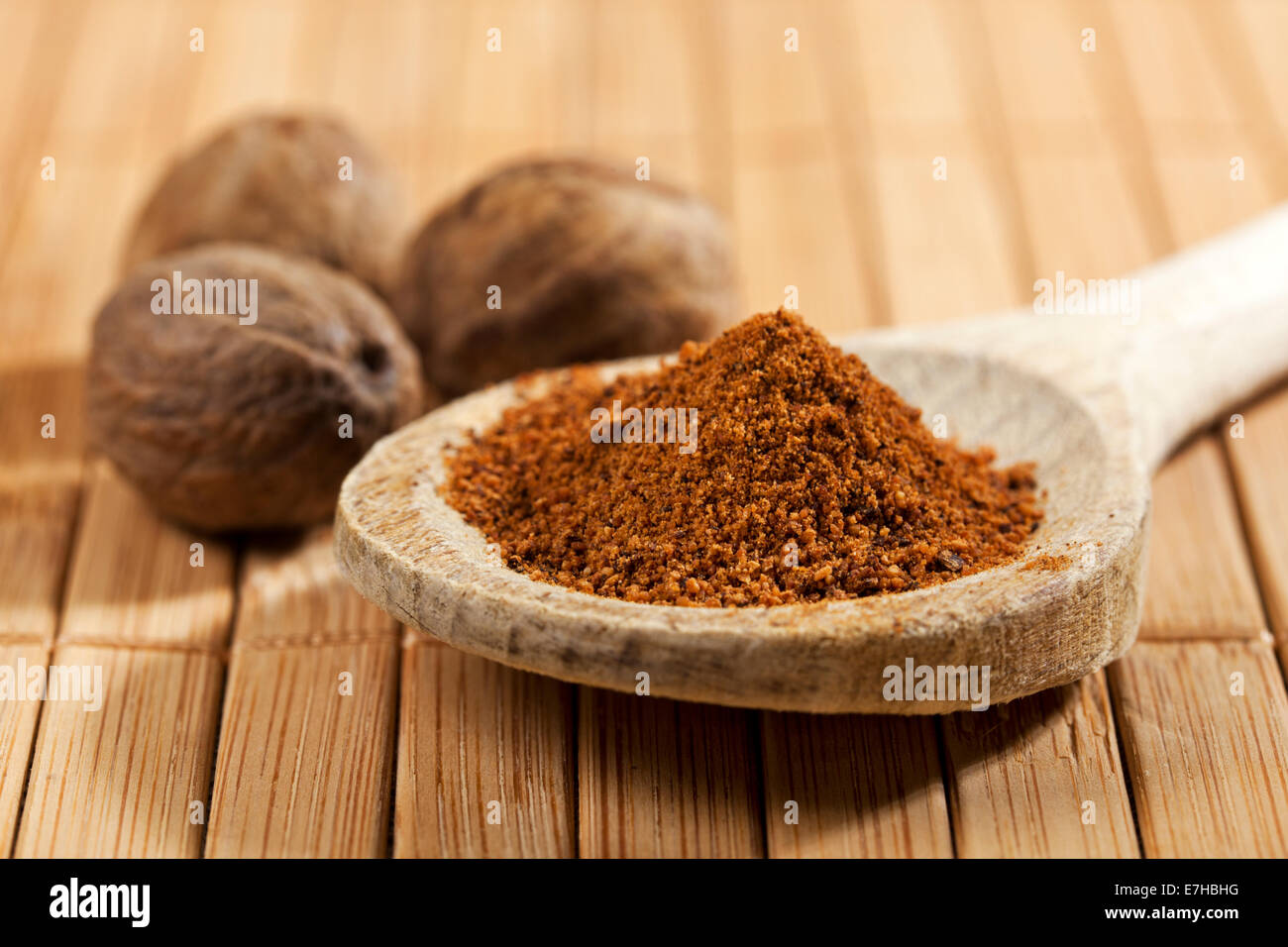Ground nutmeg on wooden spoon closeup, whole nutmeg in background Stock Photo