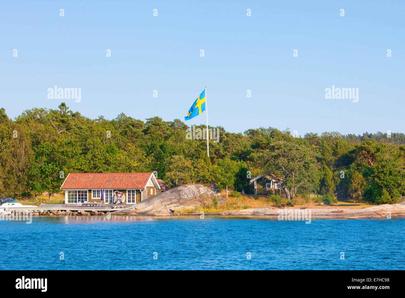 Sweden, Stockholm - House on island in archipelago with swedish flag on pole. Stock Photo
