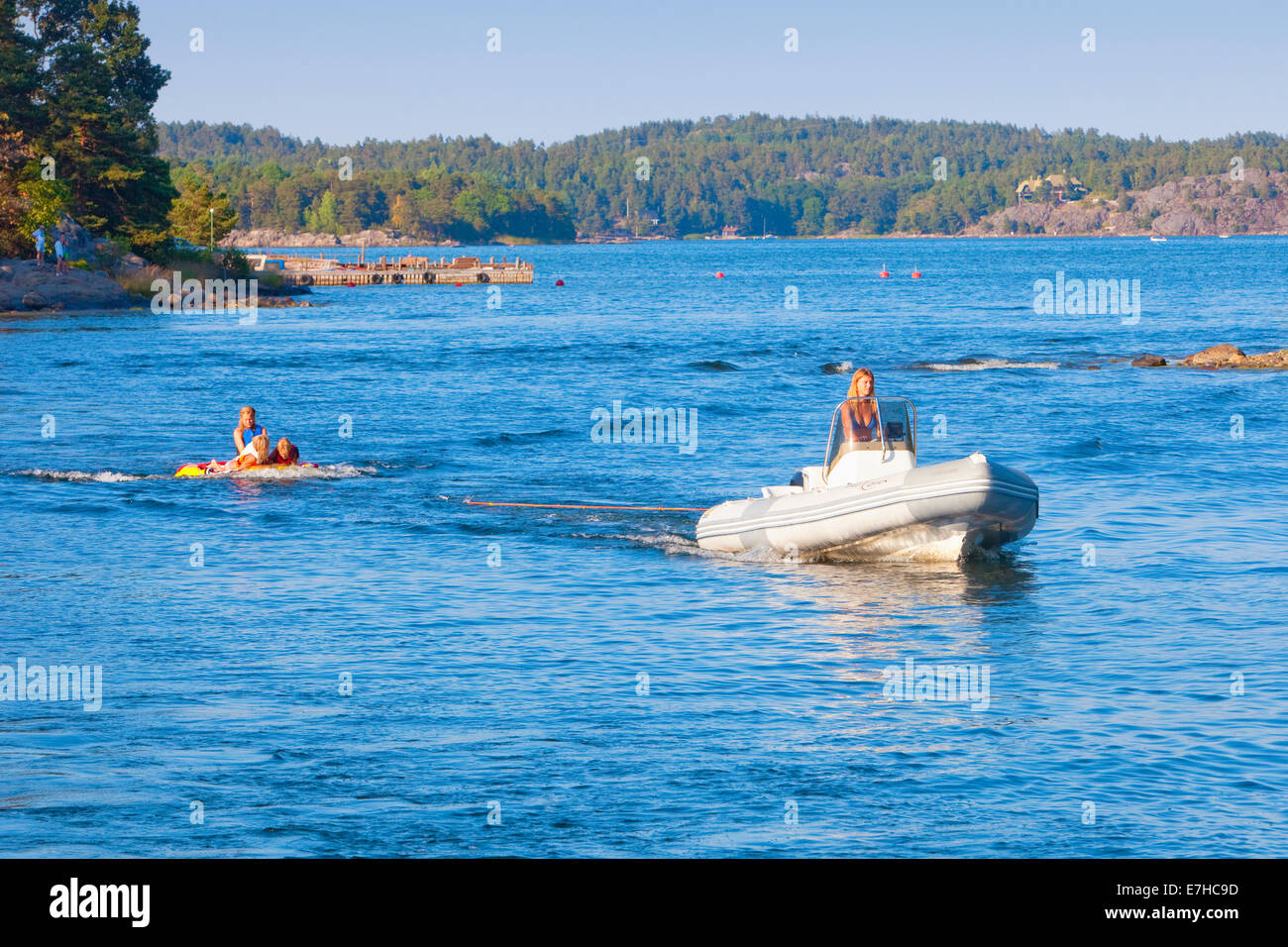 Sweden, Stockholm - Mother in motorboat pulling kids in rubberboat. Stock Photo