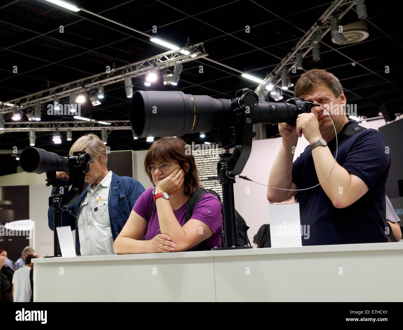 Men trying out really big lenses with woman looking very bored. Photokina 2014, Cologne, Germany Stock Photo