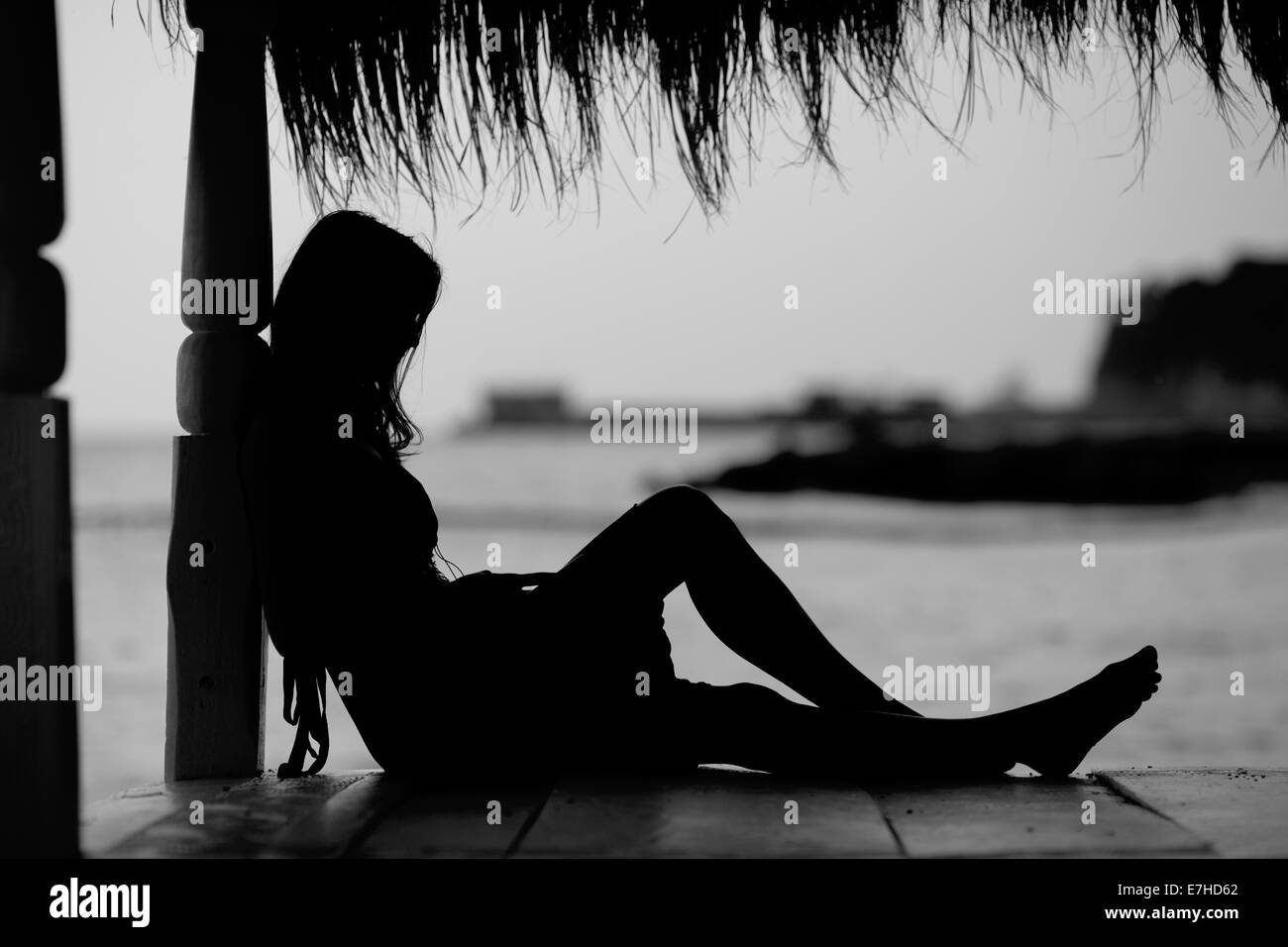 Young woman, sitting on the beach on a rainy day, listening music from ...