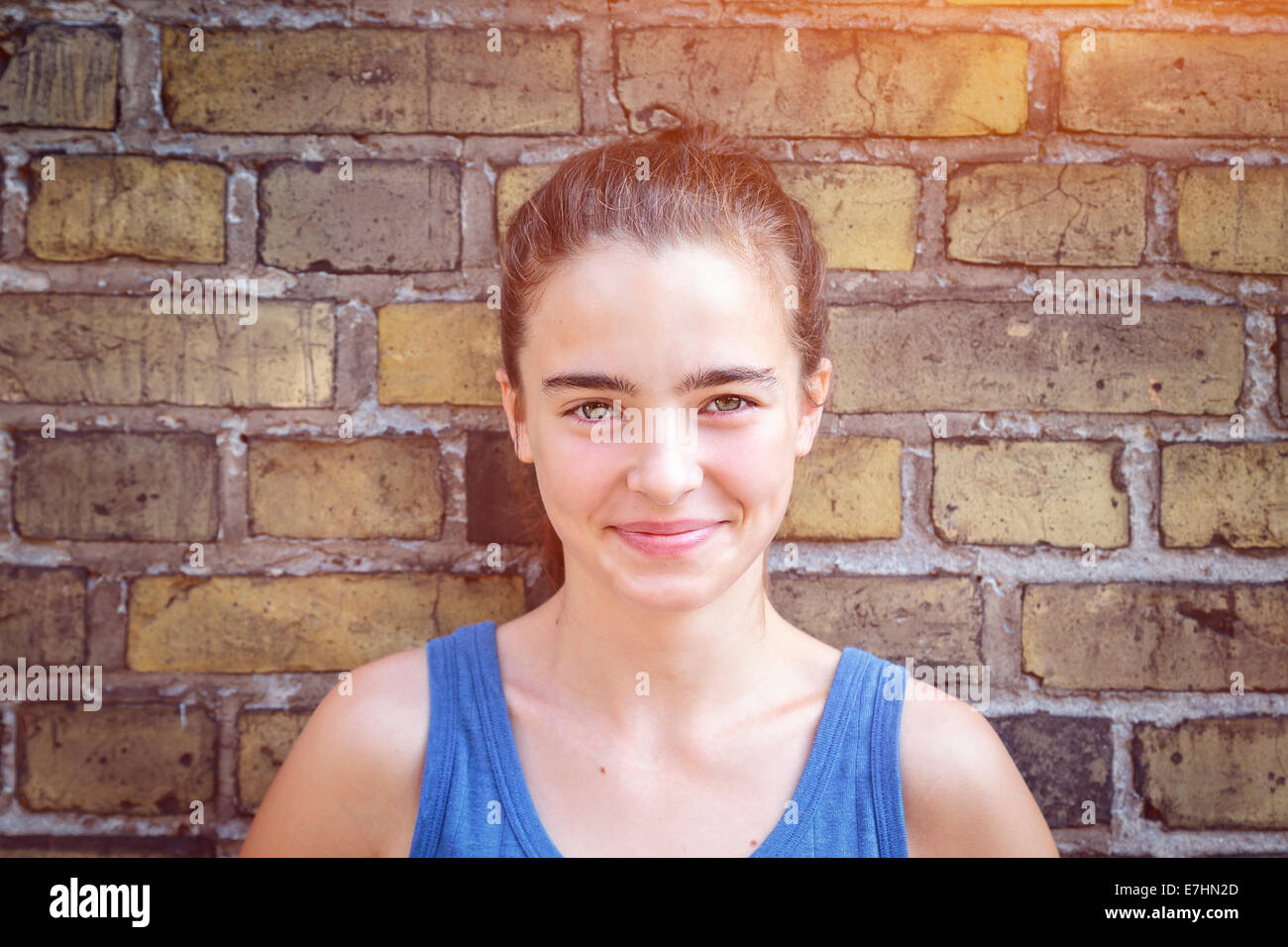 portrait of a smiling teenager girl leaning against a brick wall. Stock Photo