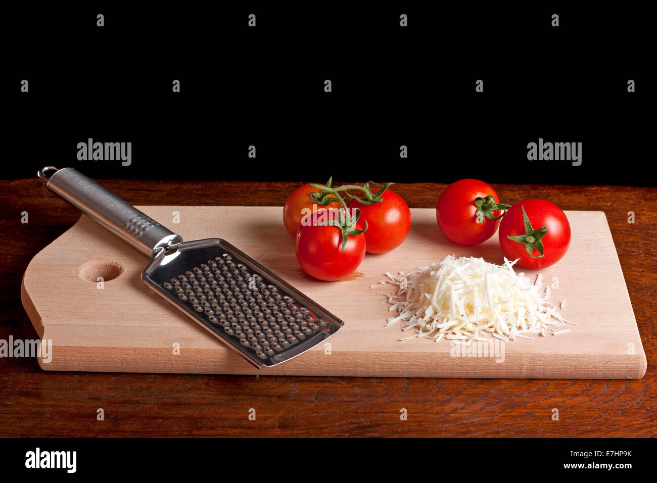 Grated cheese, grater and red tomato on a wood desk with black background Stock Photo