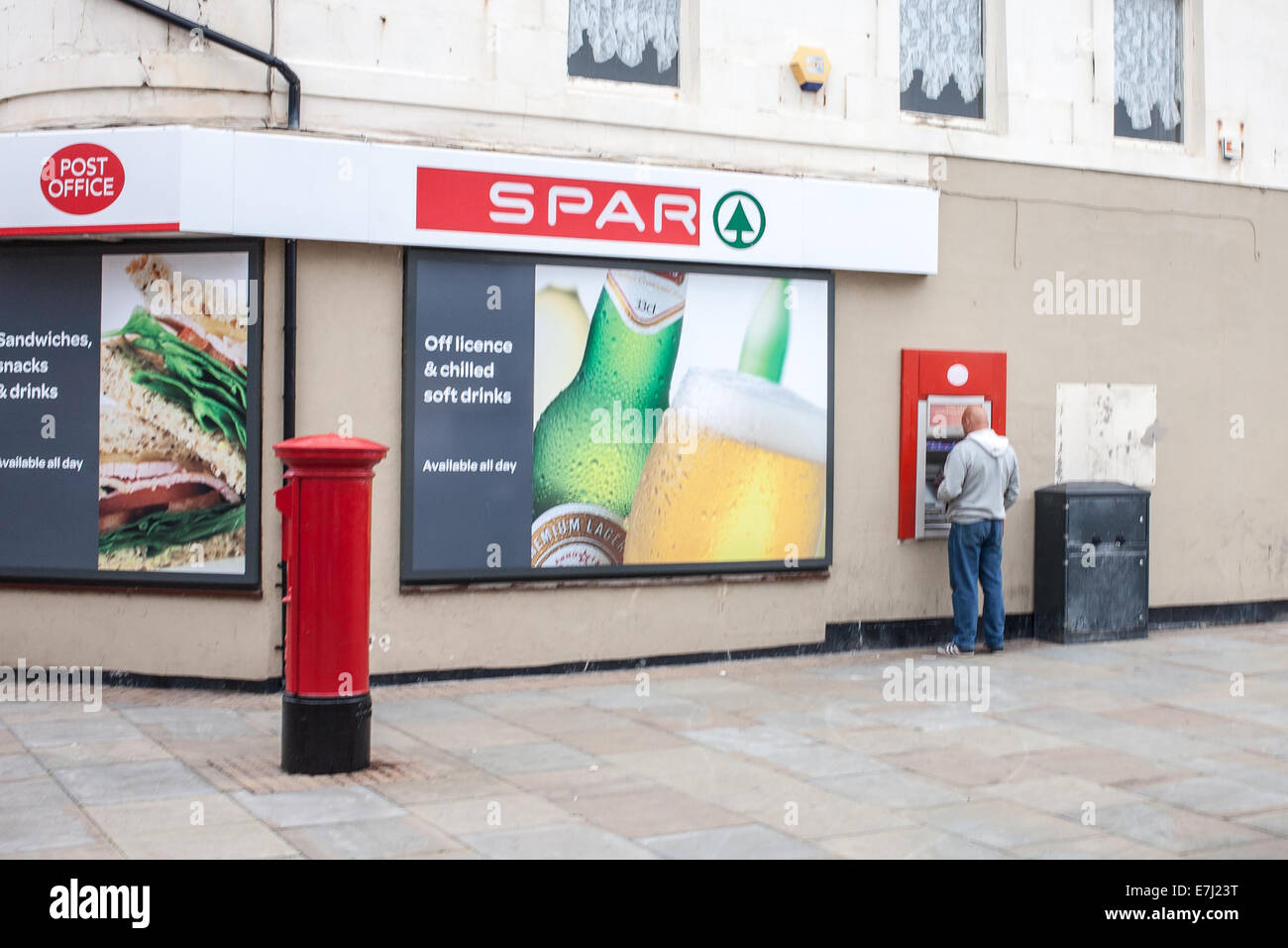 A man at a cash machine ATM at the Spar Supermarket and Post Office in Amble Northumberland UK Stock Photo