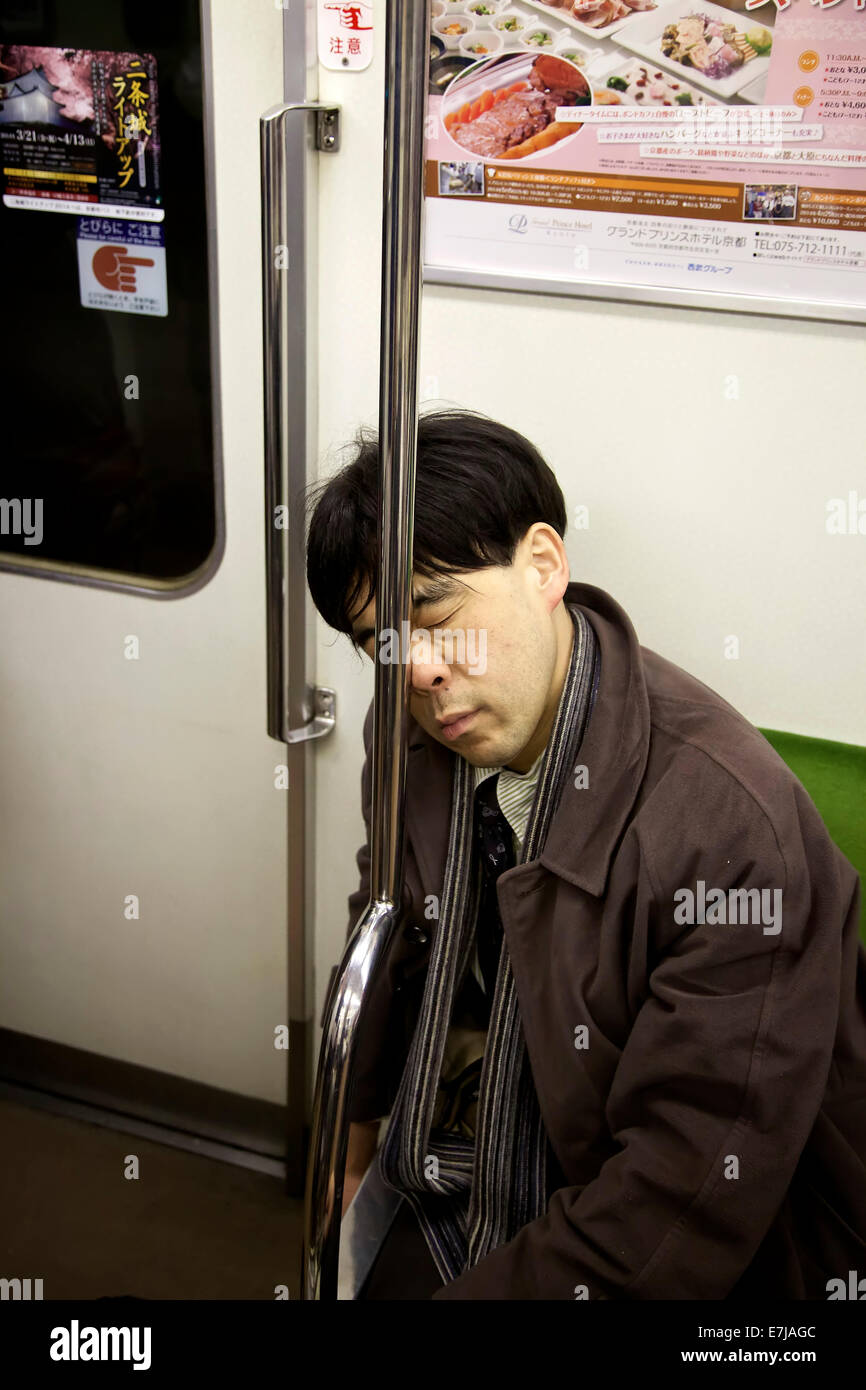 Exhausted Japanese man sleeping on subway train in Kyoto, Japan, Asia. Tired Asian businessman or manager taking a nap while commuting Stock Photo