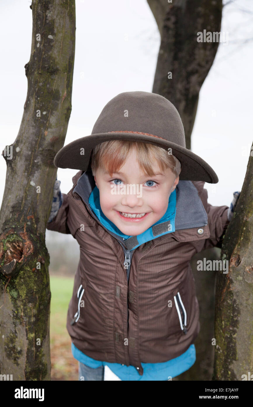 High-spirited boy, 5, wearing a hat, on a tree Stock Photo