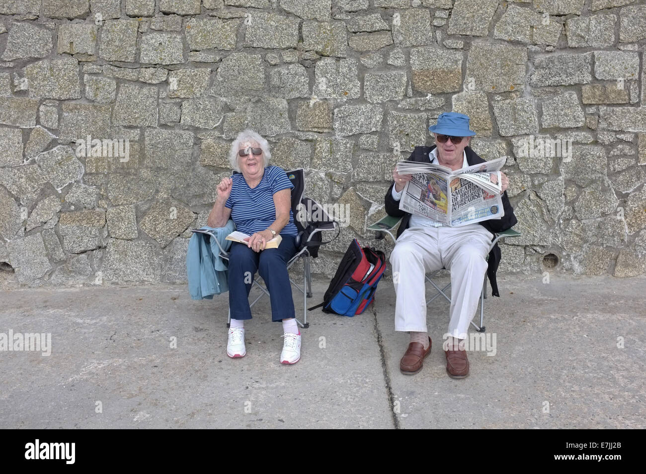 A retired couple sit by a sea wall in Falmouth, Cornwall, UK Stock Photo