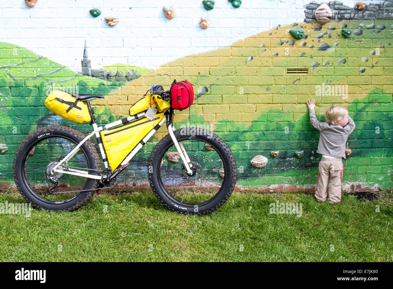 A toddler playing on a climbing wall next to a mountain Bike