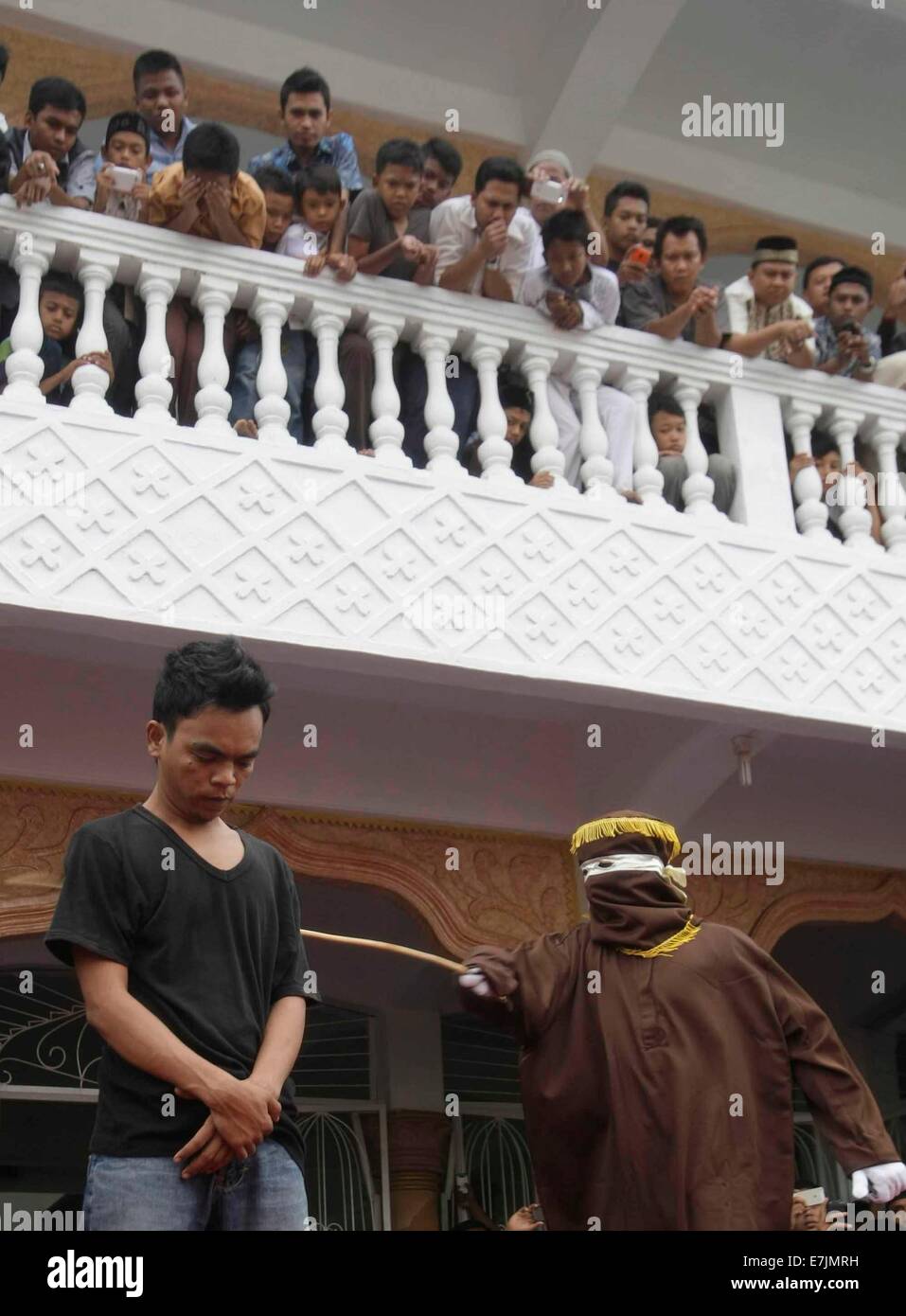Aceh, Indonesia. 19th September, 2014. A Sharia law official whips a man convicted of gambling with a rattan cane during a public caning in Aceh, Indonesia, on Sept. 19, 2014. The provincial administration of Aceh, in the north of the Indonesian island of Sumatra, has approved a law called the 'Qanun Jinayat' implemented a version of Islamic Sharia law since 2001 Credit:  Xinhua/Alamy Live News Stock Photo