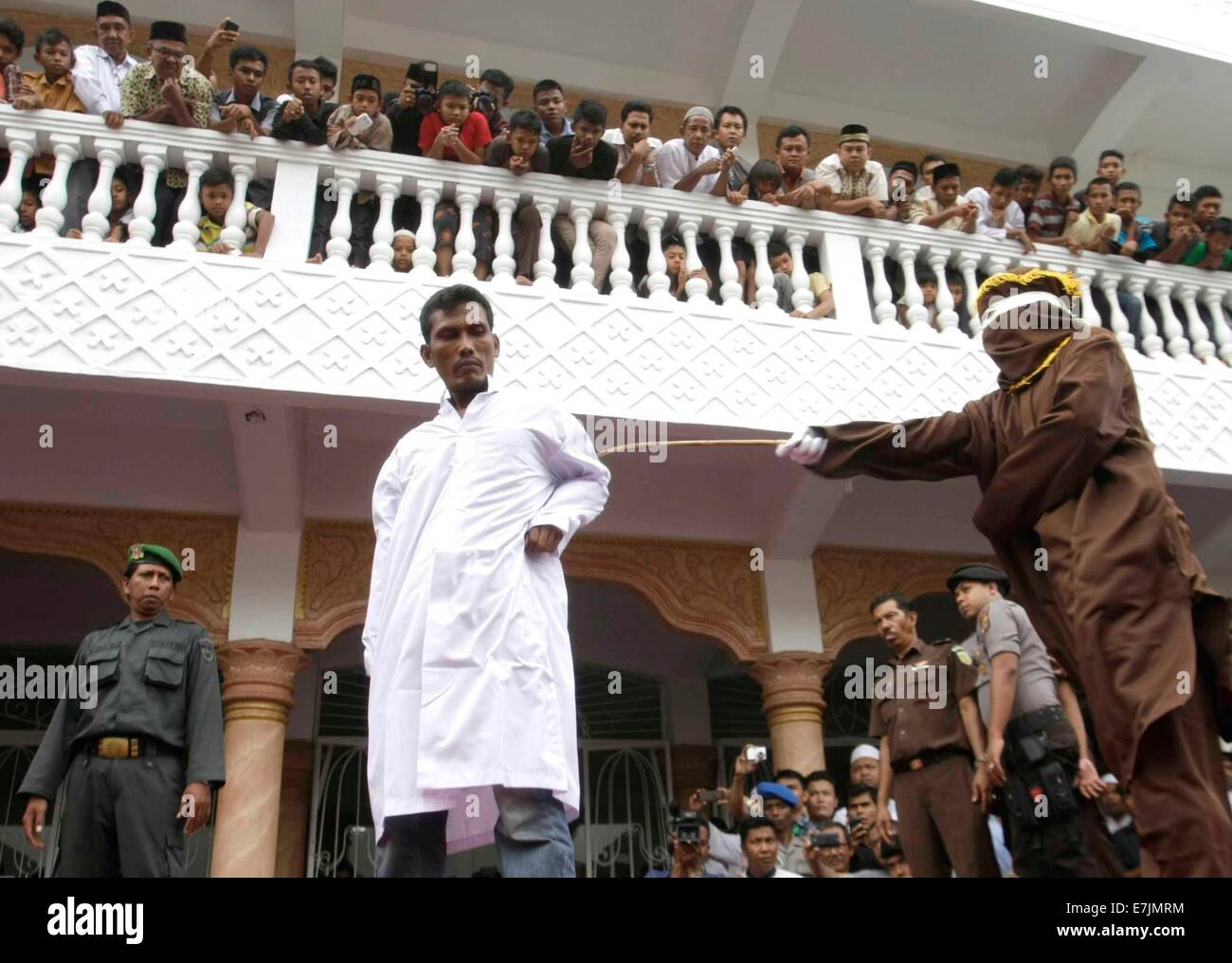 Aceh, Indonesia. 19th September, 2014. A Sharia law official whips a man convicted of gambling with a rattan cane during a public caning in Aceh, Indonesia, on Sept. 19, 2014. The provincial administration of Aceh, in the north of the Indonesian island of Sumatra, has approved a law called the 'Qanun Jinayat' implemented a version of Islamic Sharia law since 2001 Credit:  Xinhua/Alamy Live News Stock Photo