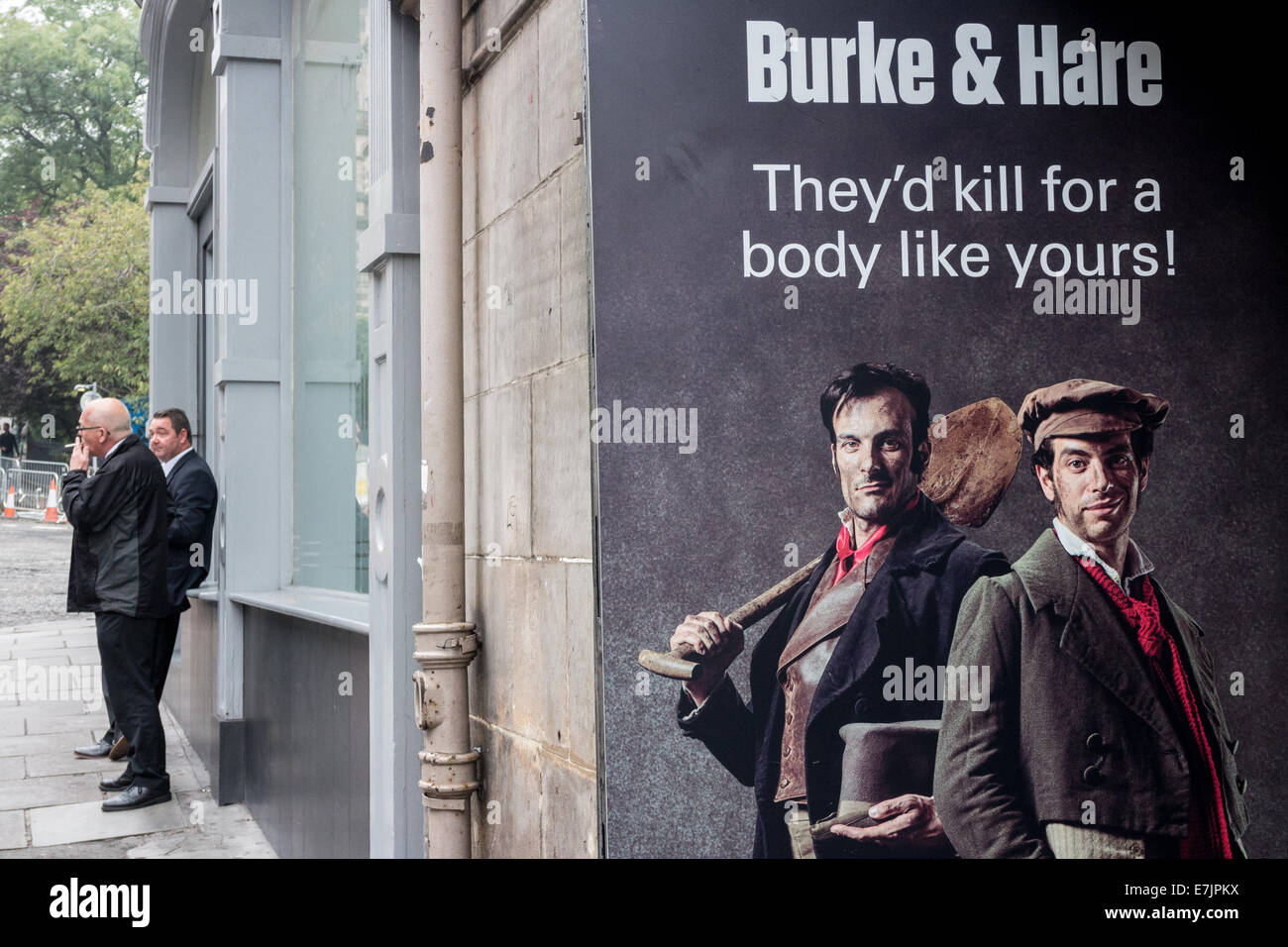 Man smoking in street near Burke and Hare billboard at the entrance to the London Dungeon, Edinburgh Stock Photo