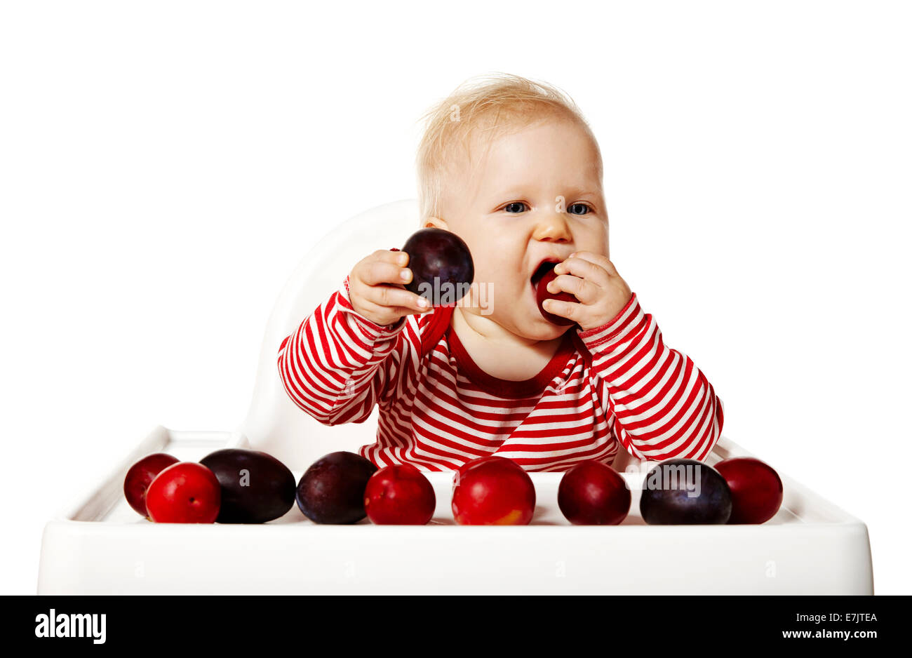 Portrait of sweet baby sitting on chair and eating plums Stock Photo