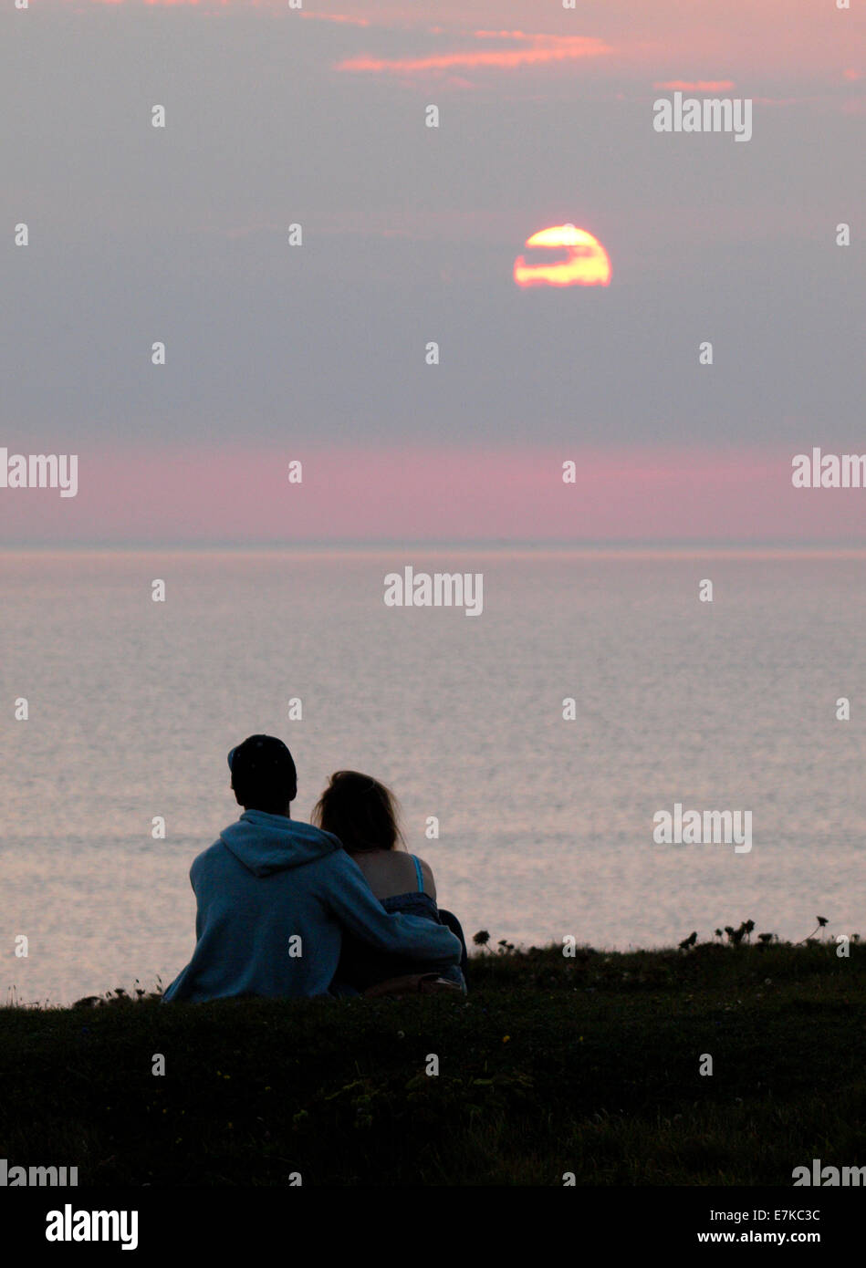 Teenage couple watching the sunset over the sea, Bude, Cornwall, UK Stock Photo