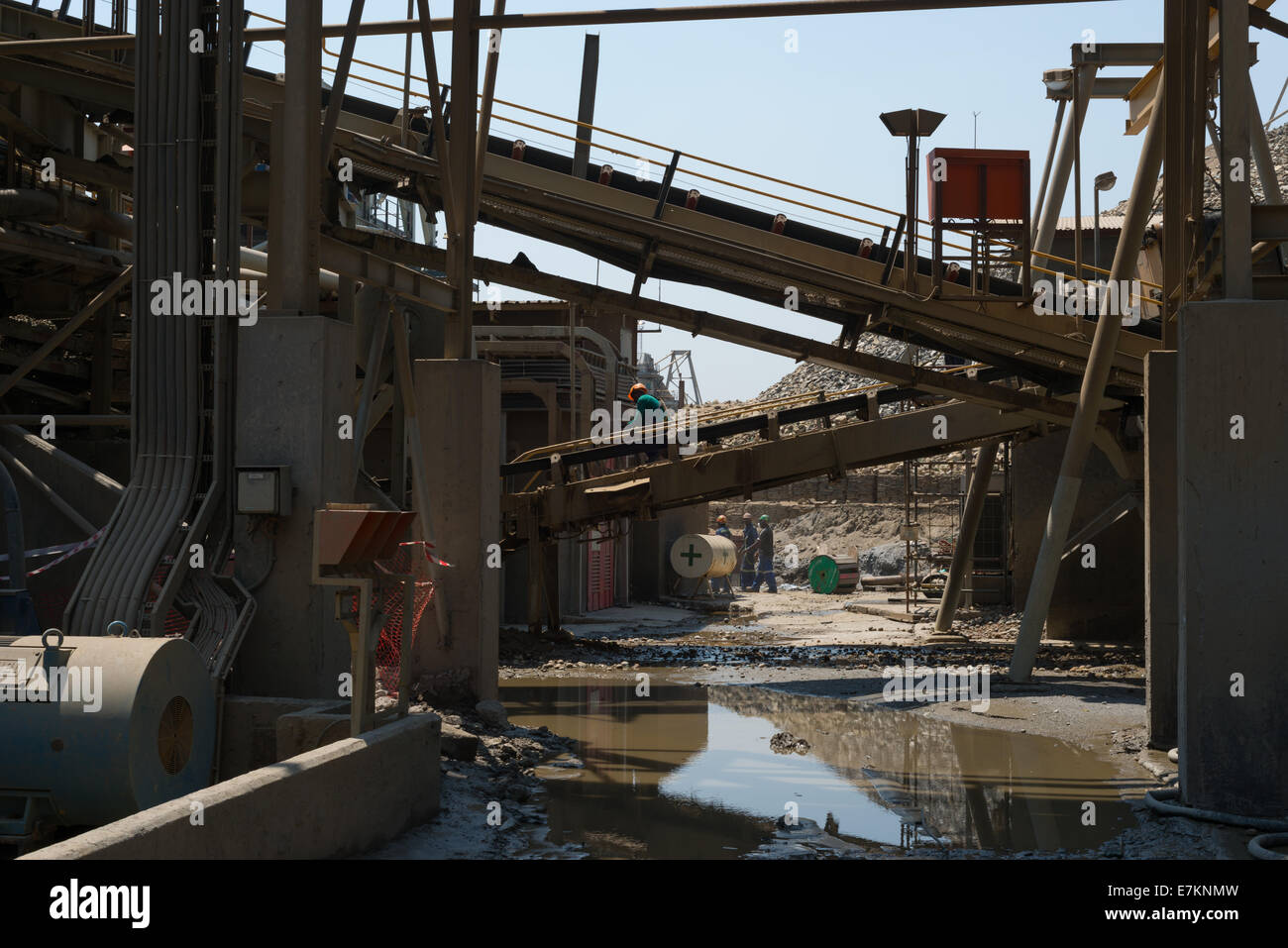 Mine workers clear a conveyor belt of rock and dirt during routine maintenance. Stock Photo