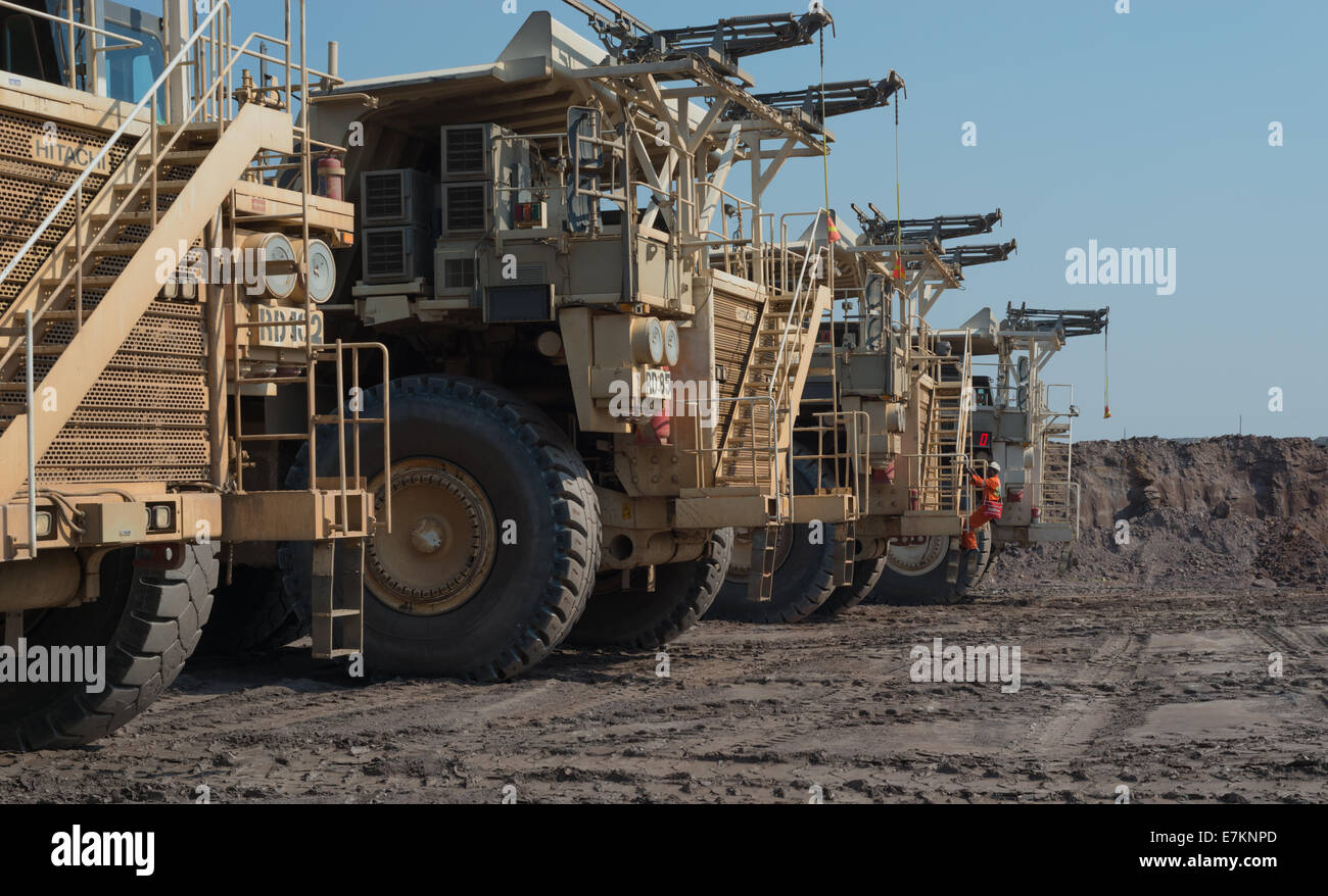 Massive Hitatchi mining trucks park up in line during shift change at an open cast African copper mine. Stock Photo