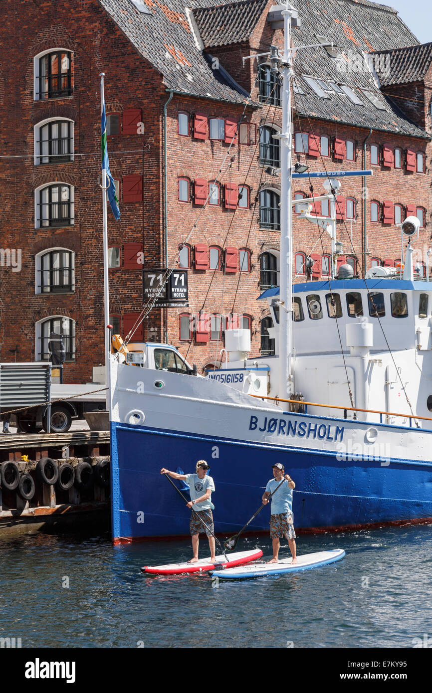 Two men stand up paddle boarding on the canal in Nyhavn, Copenhagen