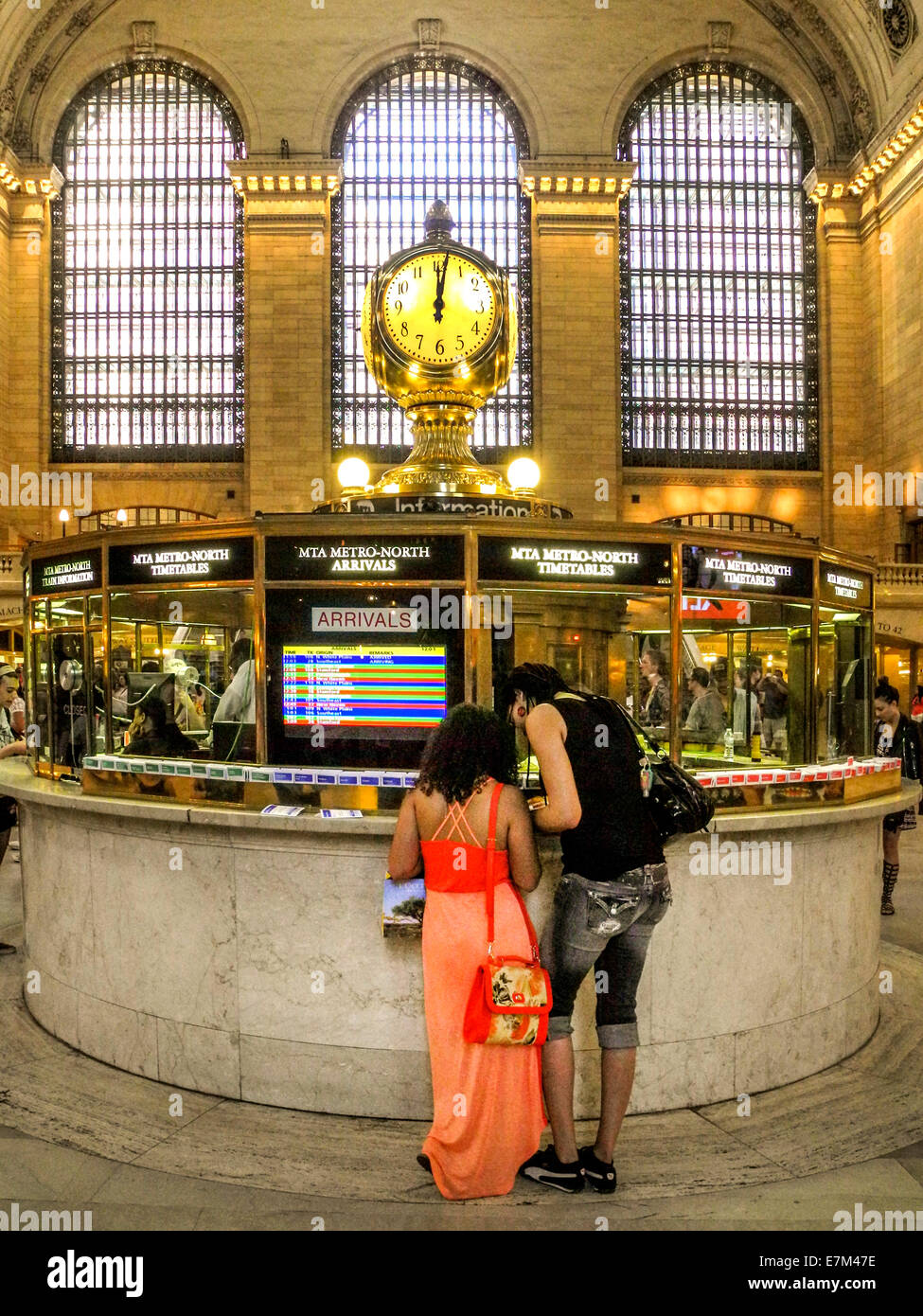 A colorfully dressed young couple read a schedule at the information booth of New York City's Grand Central Station. Note famous clock. Stock Photo