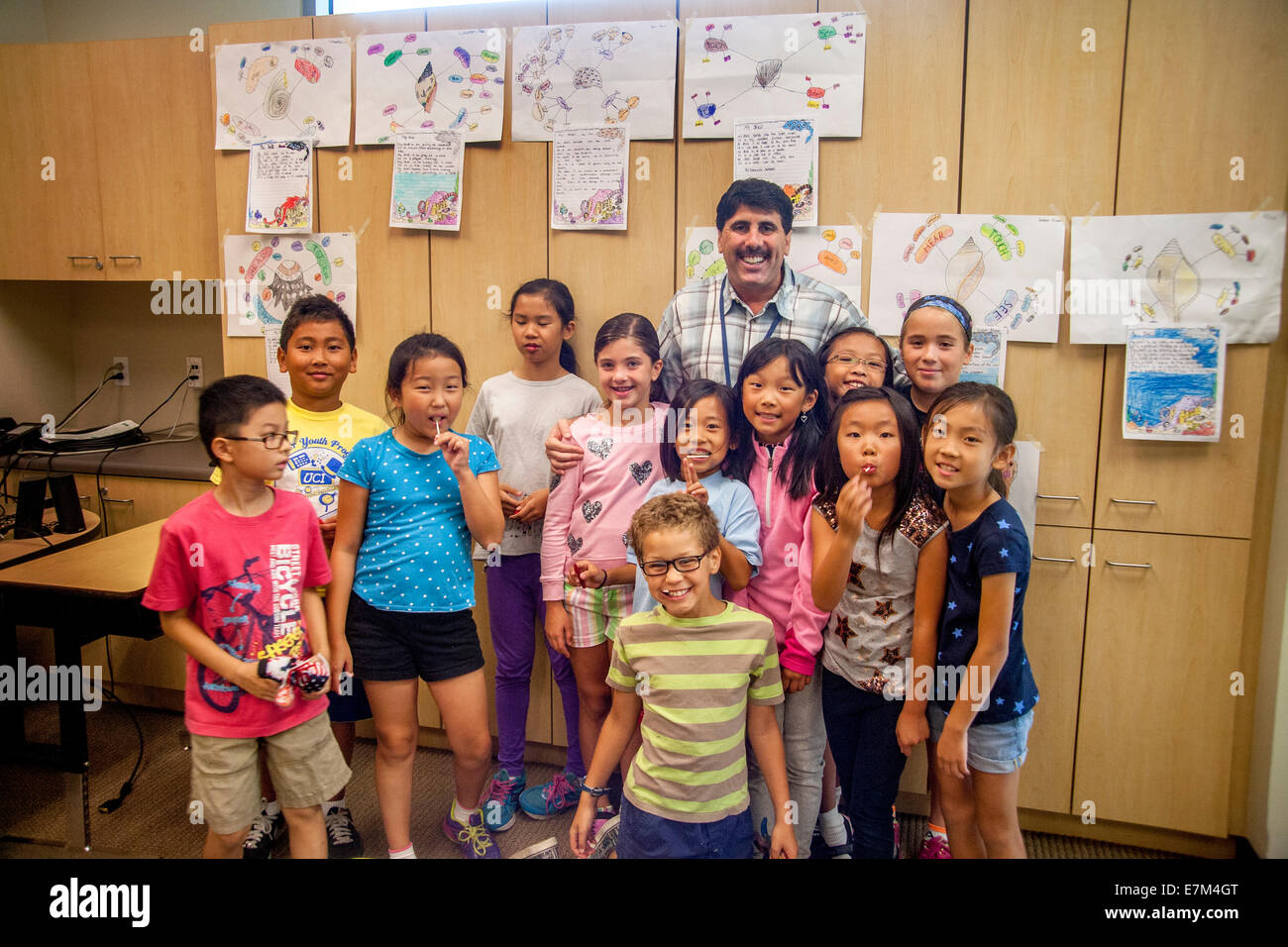 Asian, Hispanic and Caucasian elementary school students pose with their teacher at a summer writing workshop in Irvine, CA. Note yellow T shirts and drawings on wall. Stock Photo
