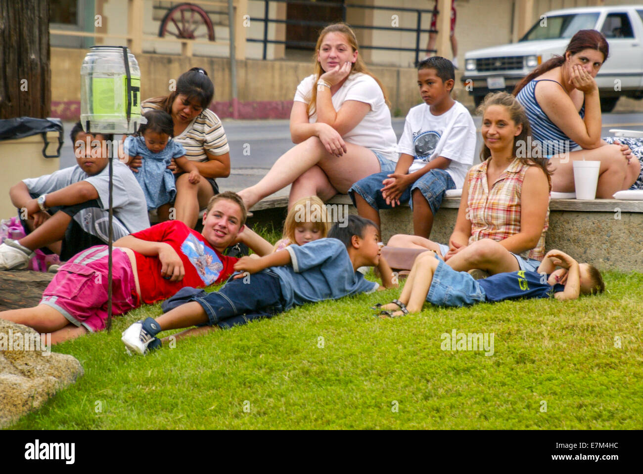 Happy multiracial local children listen to an outdoor concert in Cedar Valley, CA. Note tip jar for performer. Stock Photo