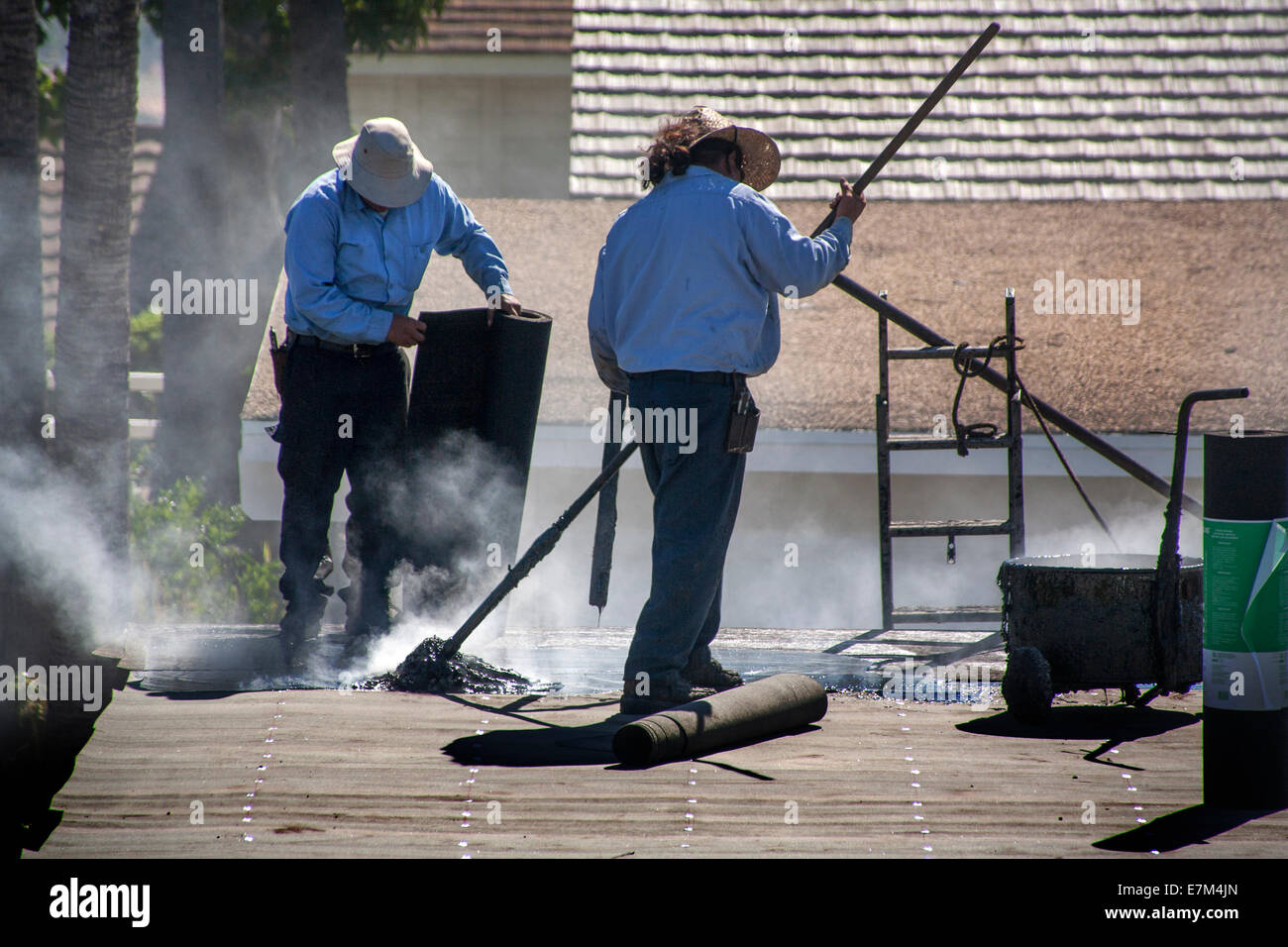 Steam rises from hot tar as Hispanic workmen replace a garage roof in Laguna Niguel, CA. Note rolls of tar paper. Stock Photo