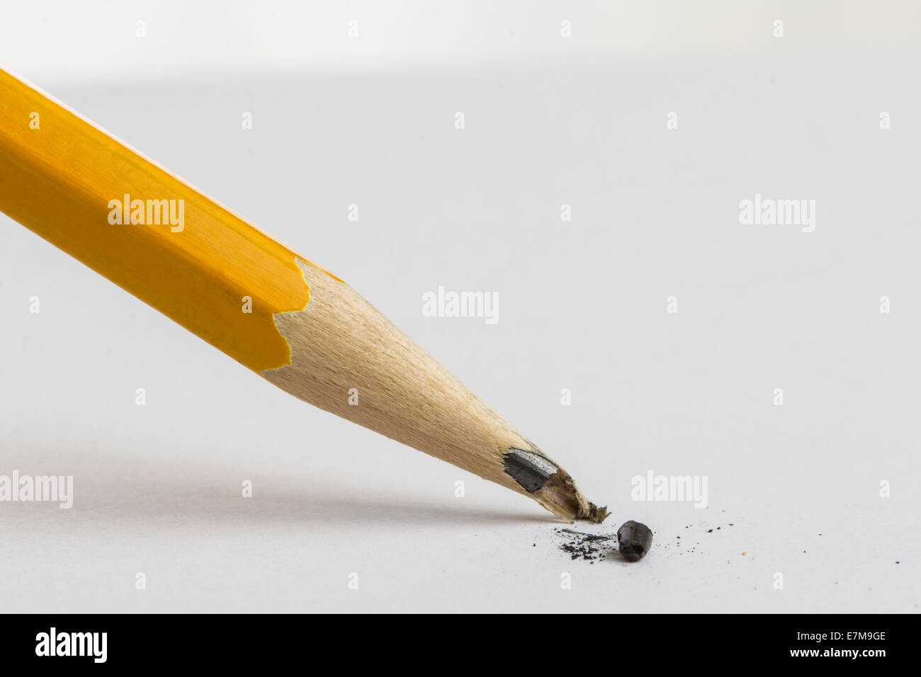 A sharpened yellow pencil over a blank sheet of paper with a broken tip. Focus on the tip of the pencil. Stock Photo
