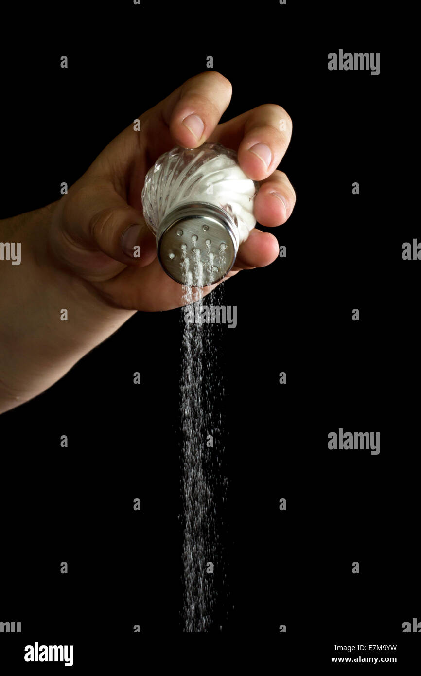 Hand adding salt using a salt shaker isolated over black background